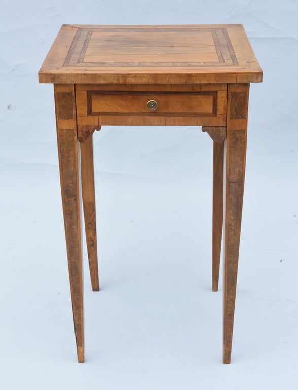 Accent table, of olive wood, having a square top decorated with banding, on apron with corner brackets, its single frieze drawer with similar inlay, raised on burl-inlaid, tapering square legs.