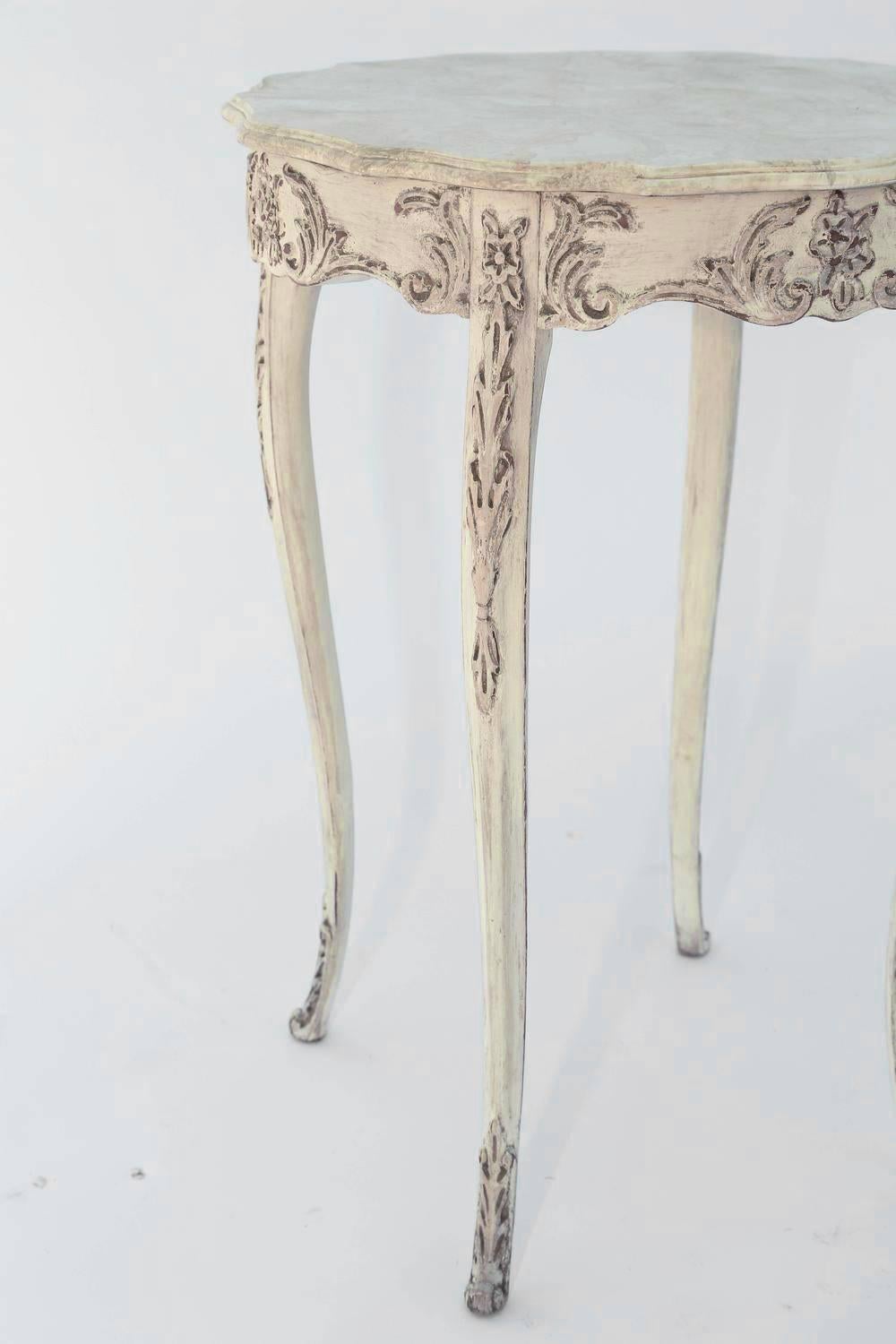 Table, having a round molded top with serpentine edge in faux mabre, on foliate-carved, scalloped apron, raised on delicate cabriole legs, each with festooned knees and feet. 

Stock ID: 6158.