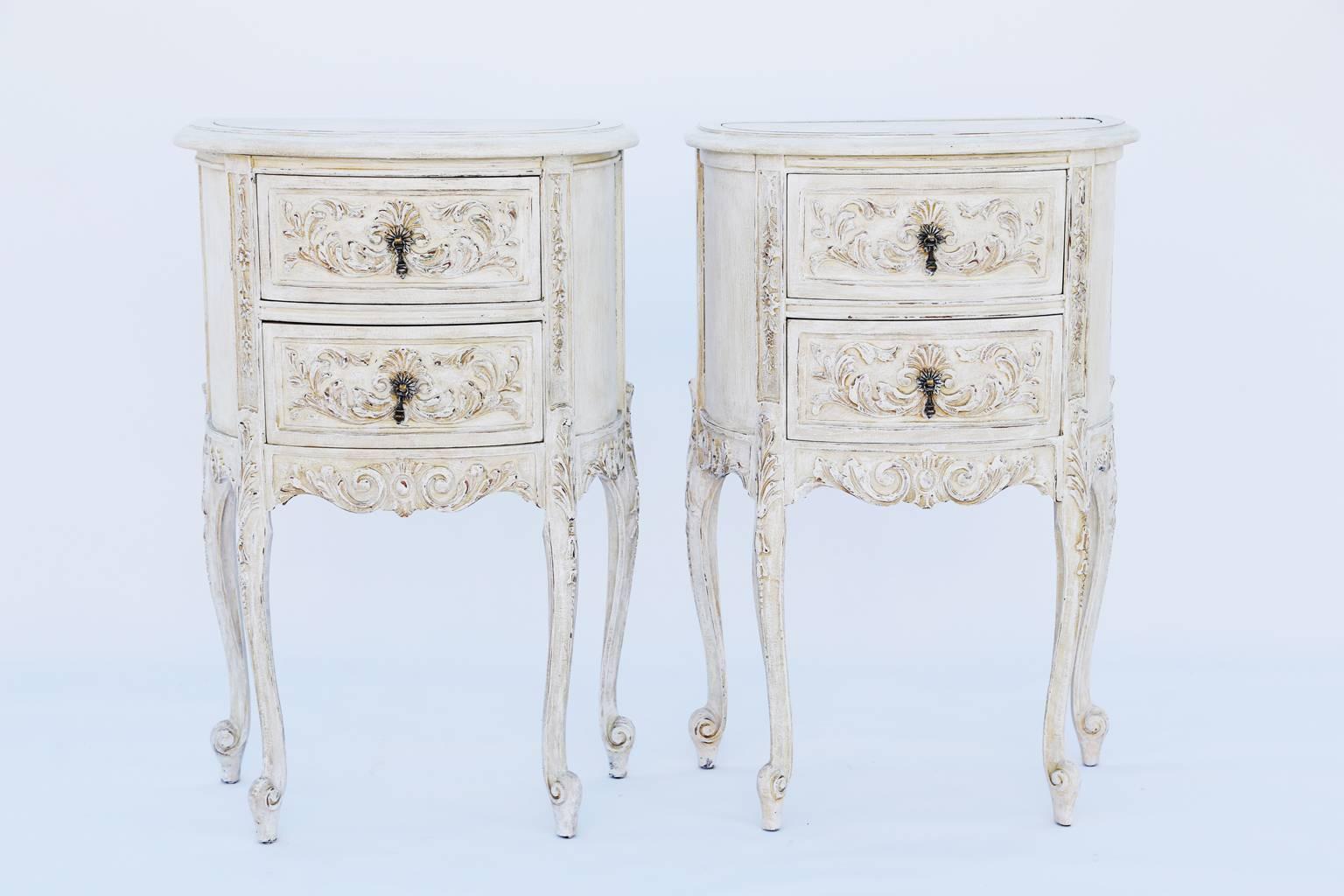 Pair of bedside commodes, in the Louis XV style, each chest having a demilune top inset with antiqued mirror, with molded edge, on two stacked drawers, carved with a palmette and scrolling acanthus, flanked by foliate-carved stiles, on similarly