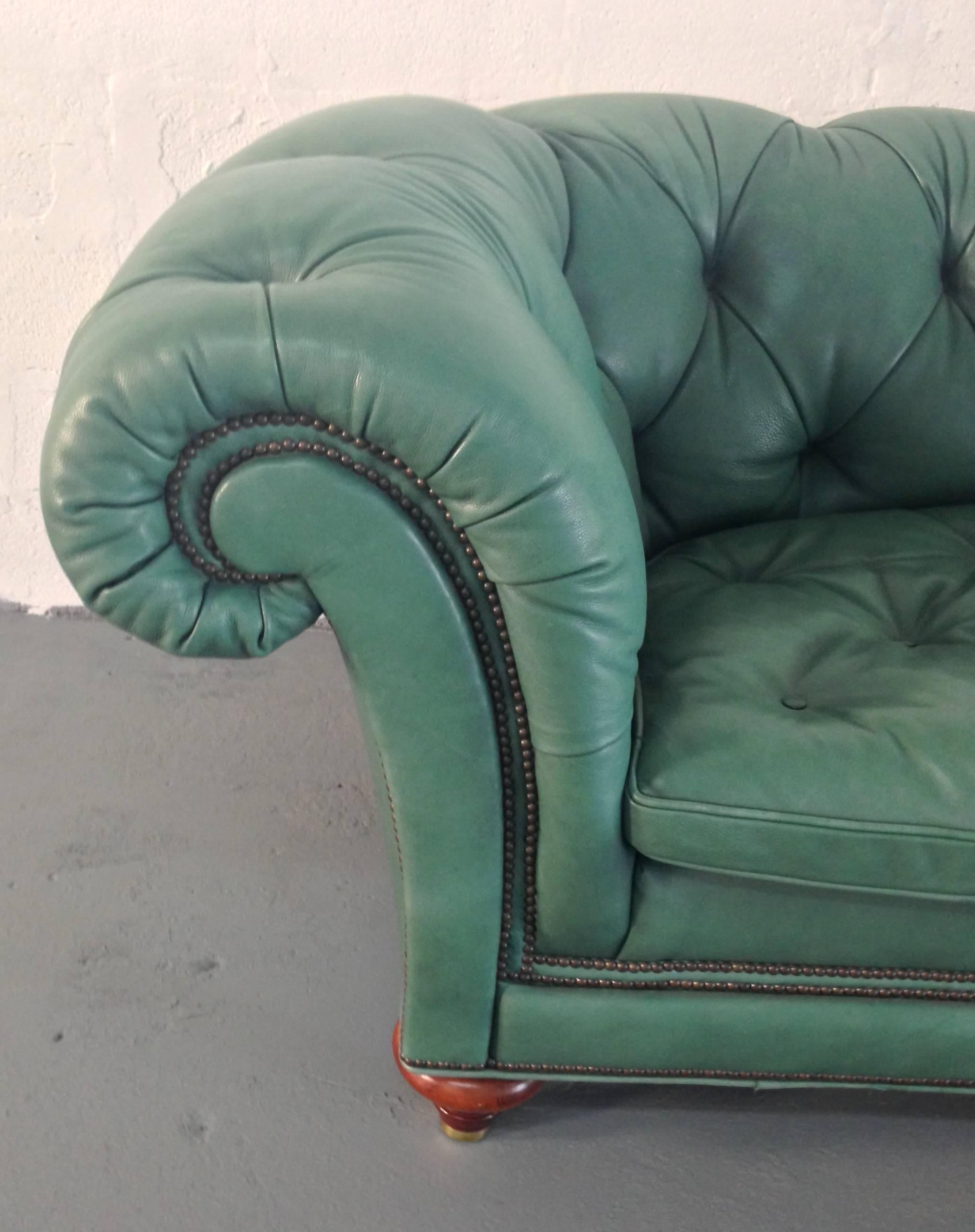A large, comfortable and beautiful chesterfield sofa with original buttoned English green leather upholstery, brass nailhead trim, oversized scrolled arms and sculpted mahogany wood feet.