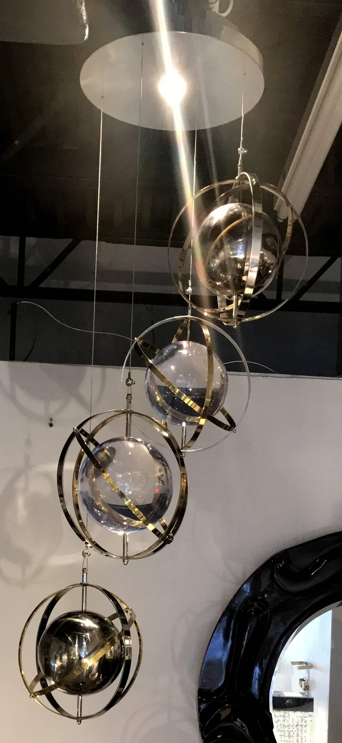 A custom-made pair of flush mount stainless steel, brass and Lucite chandeliers with armillary spheres on adjustable cables. The cables can be shortened or lengthened as desired. The maximum drop 60 inches and the minimum drop 20 inches.