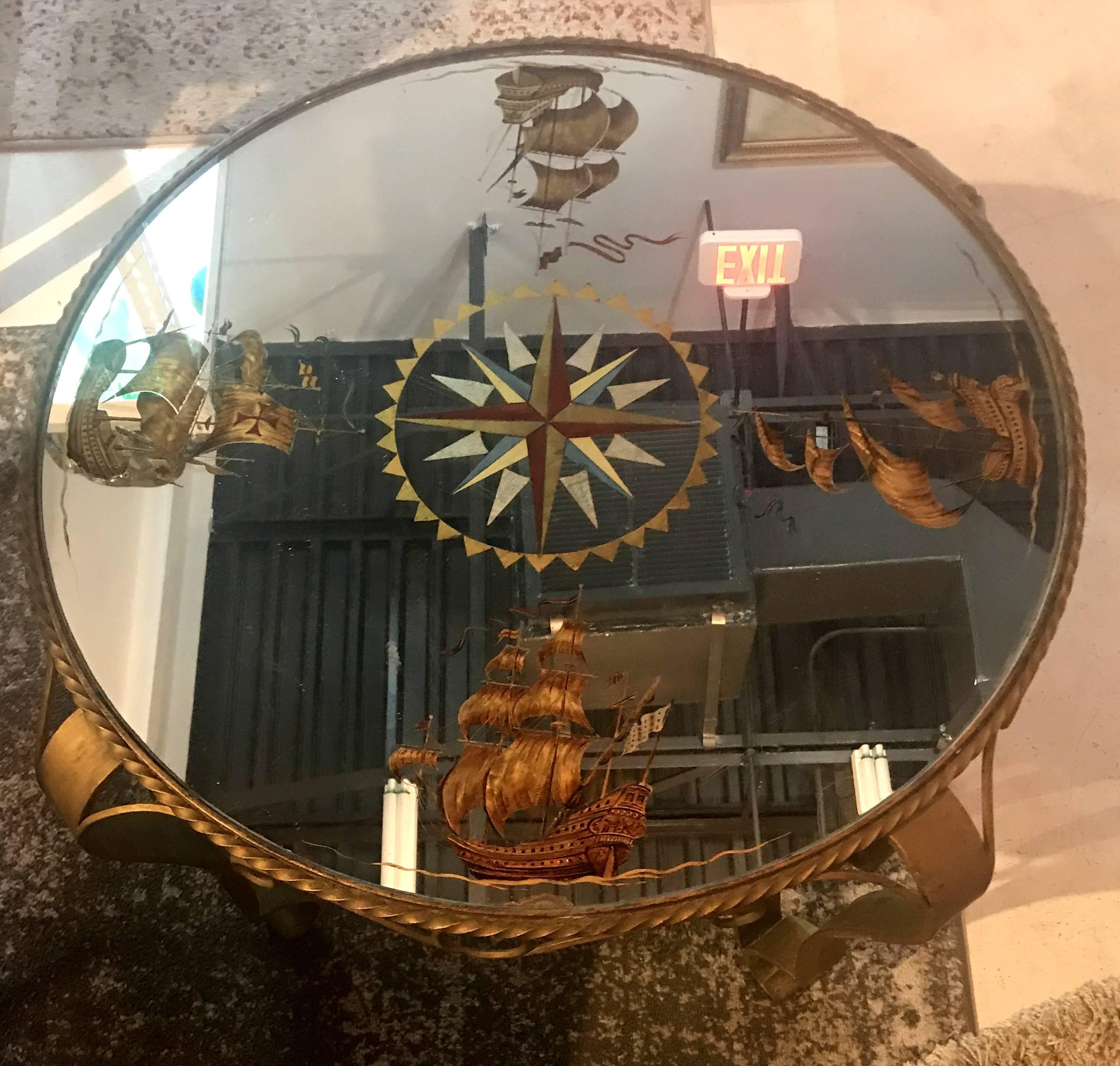 Chic French 1940s round coffee table. A heavily scrolled gilt wrought iron with twisted gilt iron details, form the base. A beautiful nautical themed compass in églomisé´ mirror top this charming table.