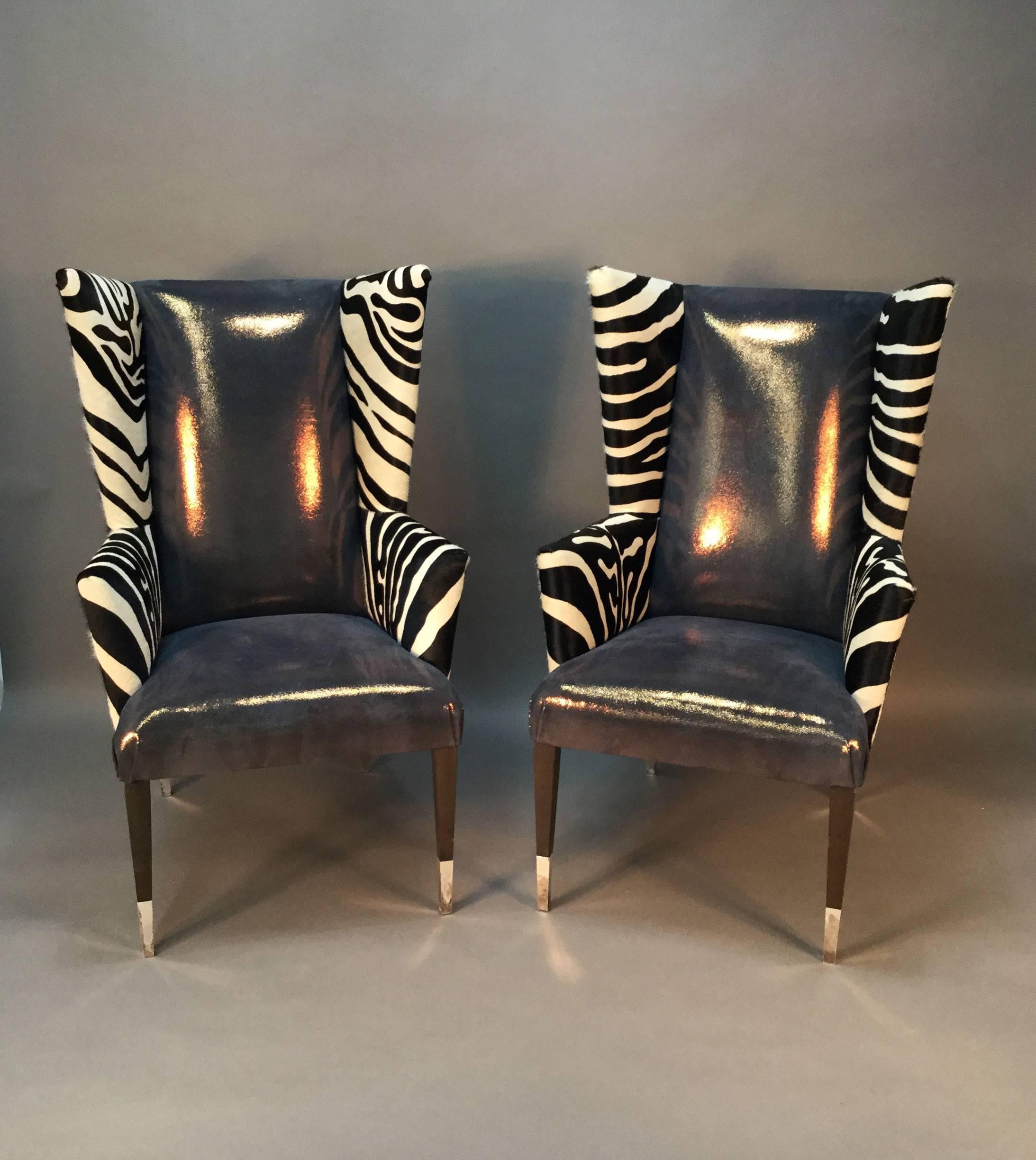 This is an amazing pair of wingback chairs by Sally Sirkin Lewis for J. Robert Scott. Back and arms upholstered in zebra print cowhide. Front upholstered in faux shagreen. Stained legs with silver plated sabots. Incredible statement pieces.