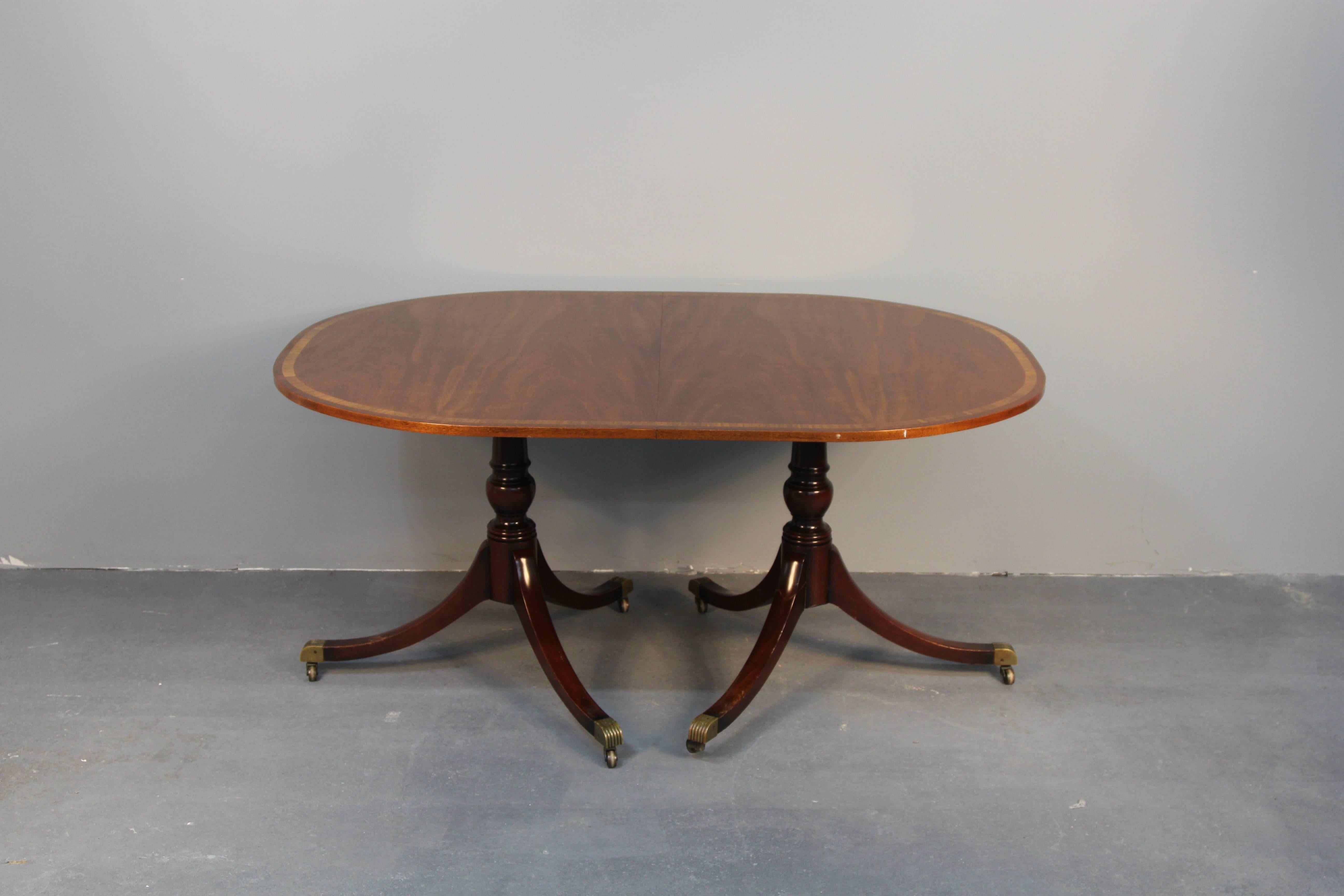 Early 1900s mahogany double pedestal dining table. With oval ends, two leaves, inlaid banding at edge of top, and brass caster capped feet. 42