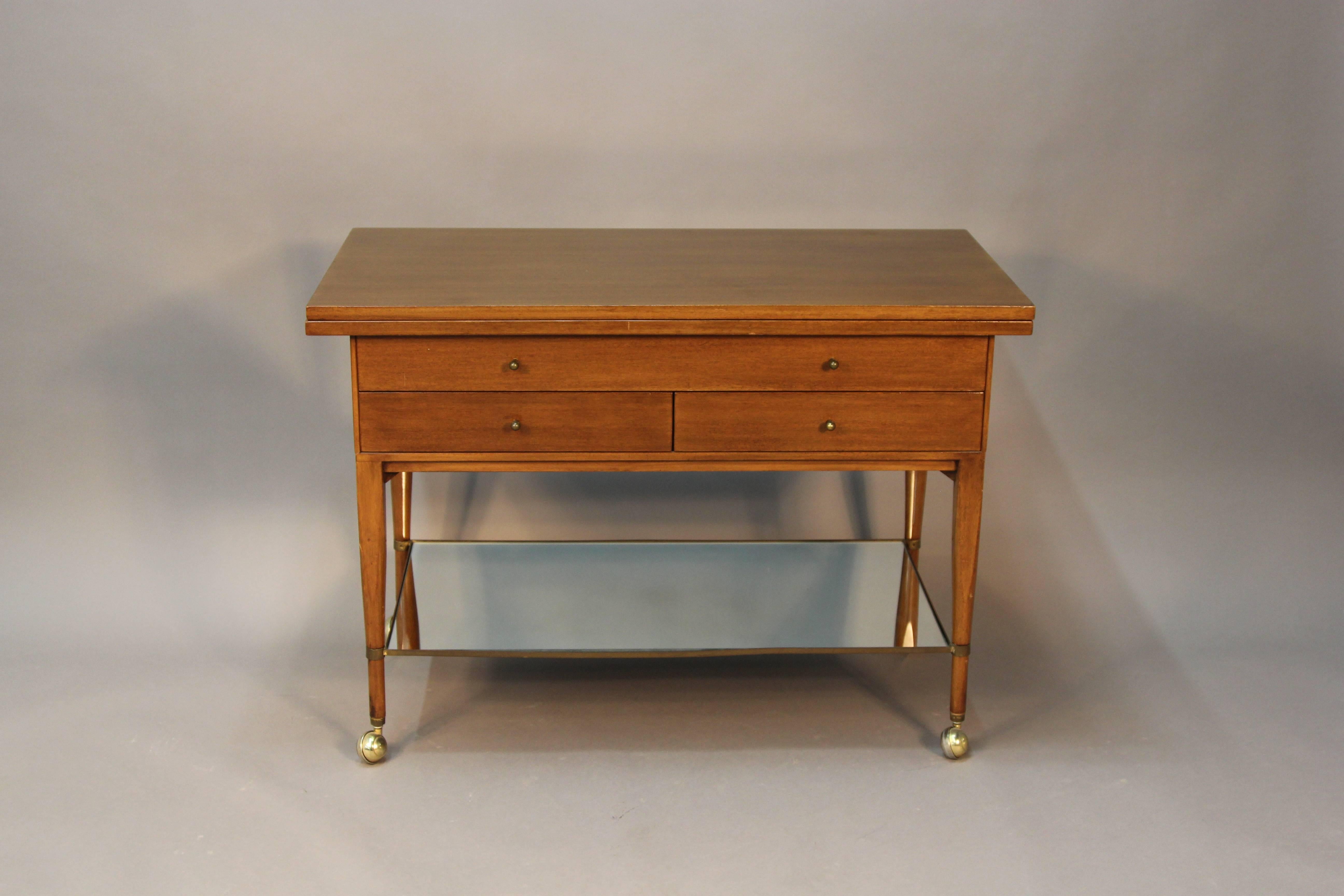 Paul McCobb designed for The Calving Group wooden bar cart with brass shelf. Currently contains new mirror, but most like once contained a travertine marble insert. Brass castors and baby pull knobs. Three drawers and extendable top.