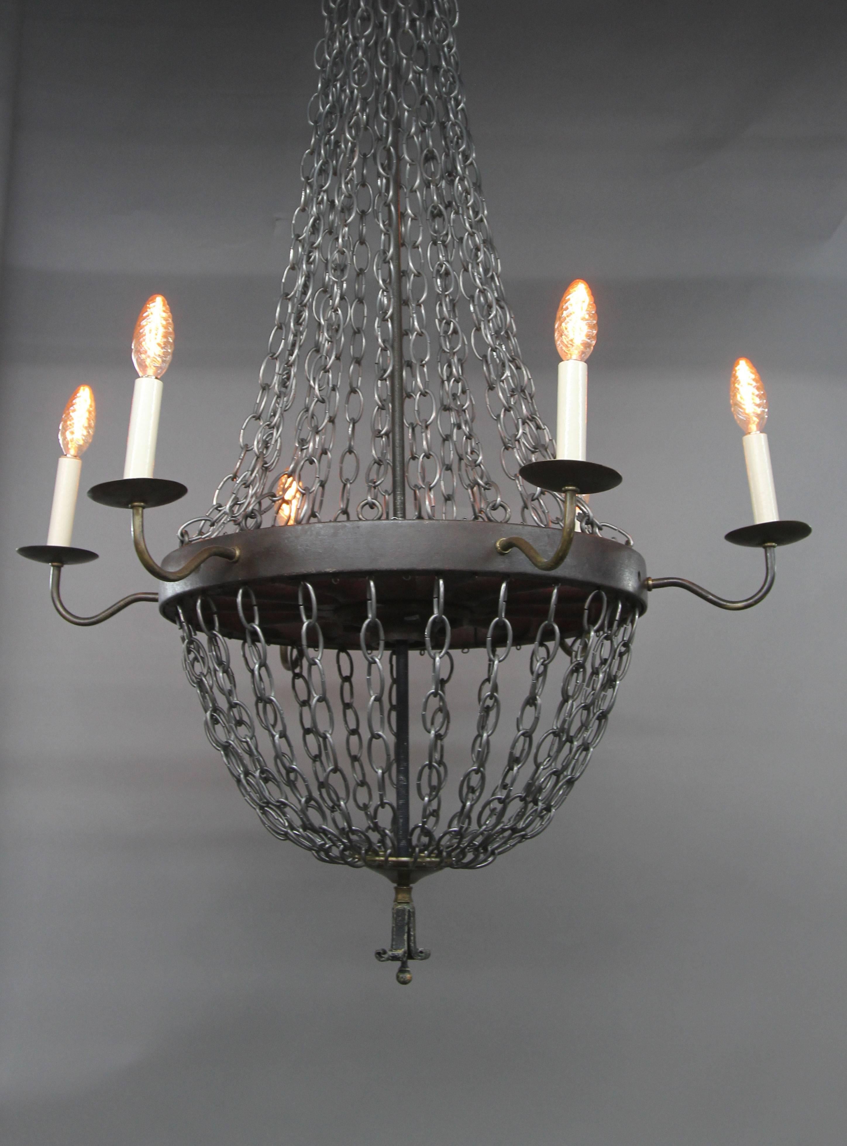 Unique and impressive, this superbly handcrafted six-arm chandelier features steel chains linking to a distressed Industrial wheel base reminiscent of medieval times. Six brass arms fitted with brass holders and amber candle flame bulbs. Brass