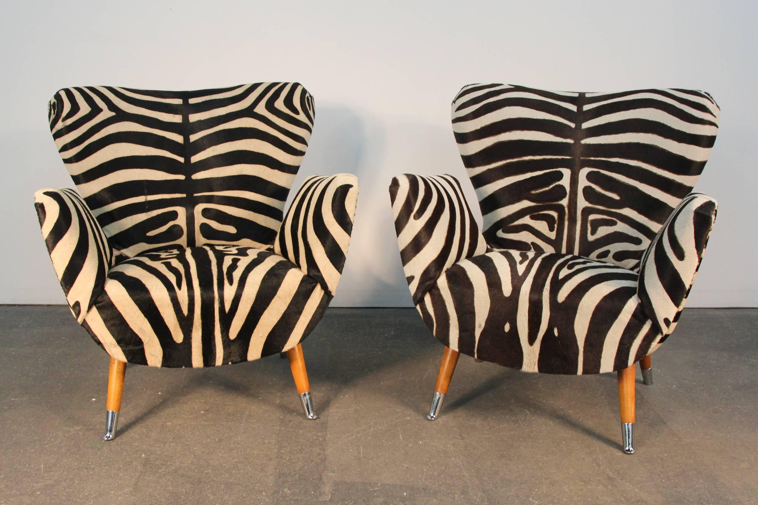 Cowhide upholstered chairs with zebra print. Butterfly backs and flared arms. Wooden legs with chrome sabots. Nailhead detail on back.