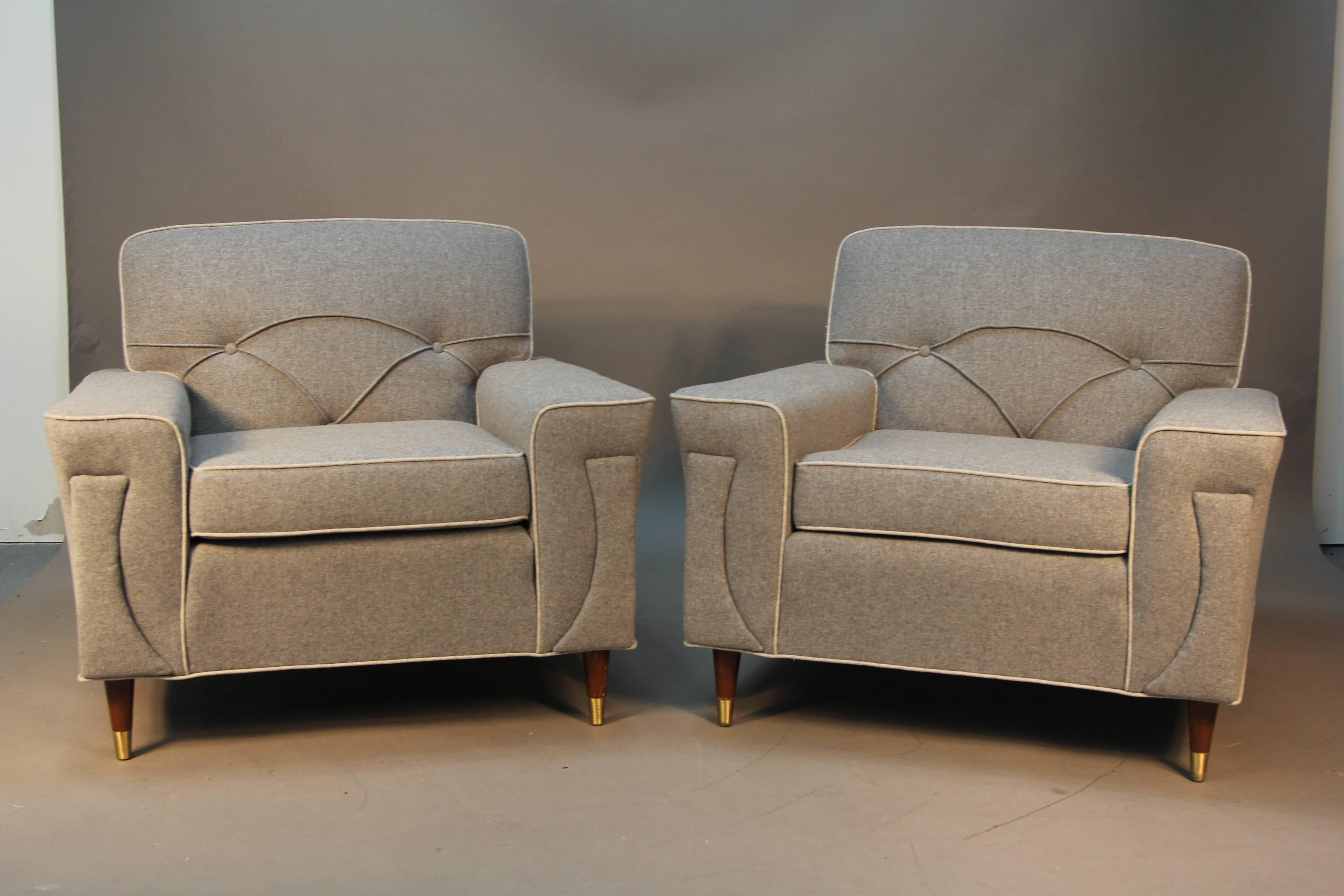 Gorgeous newly upholstered pair of Mid-Century Modern club chairs. Upholstered in grey wool with lighter contrast piping. Very unique tufting and seem details. Wooden legs with brass sabots. Very comfortable.