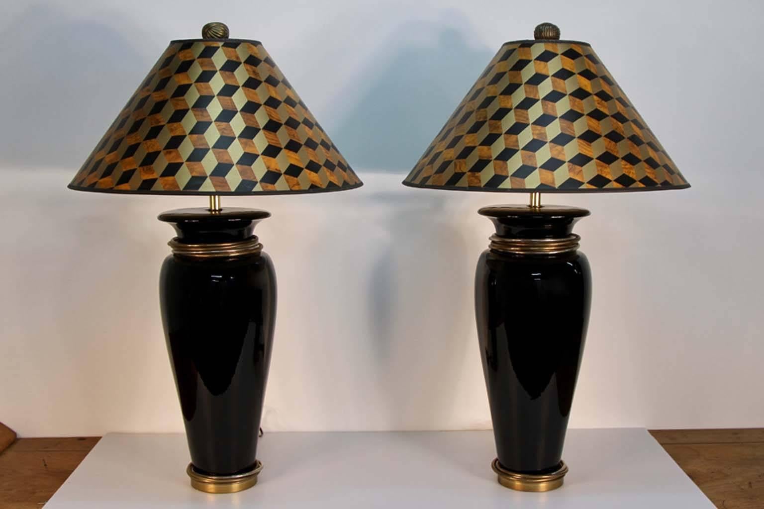 Pair of Chapman table lamps with black ceramic vase form lamps. Tonal metal loose rings at the neck and base, retaining their original optical grid pattern paper shades, substantial knob finials, and dated labels.