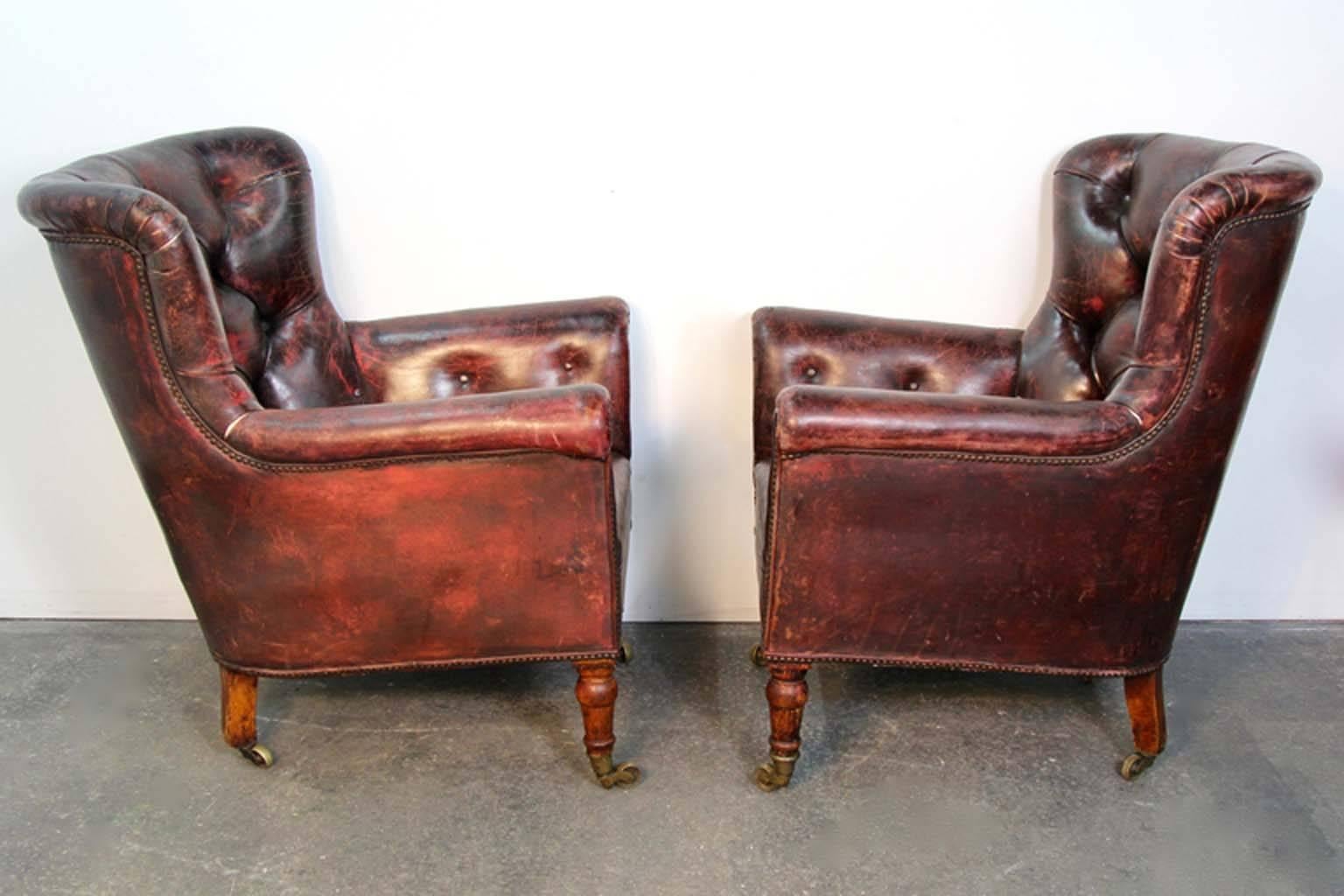 Stunning pair of antique 19th century leather club armchairs. Nailhead trim. Original tufted leather worn to fabulous patina. Brass castors. Turned front legs.
