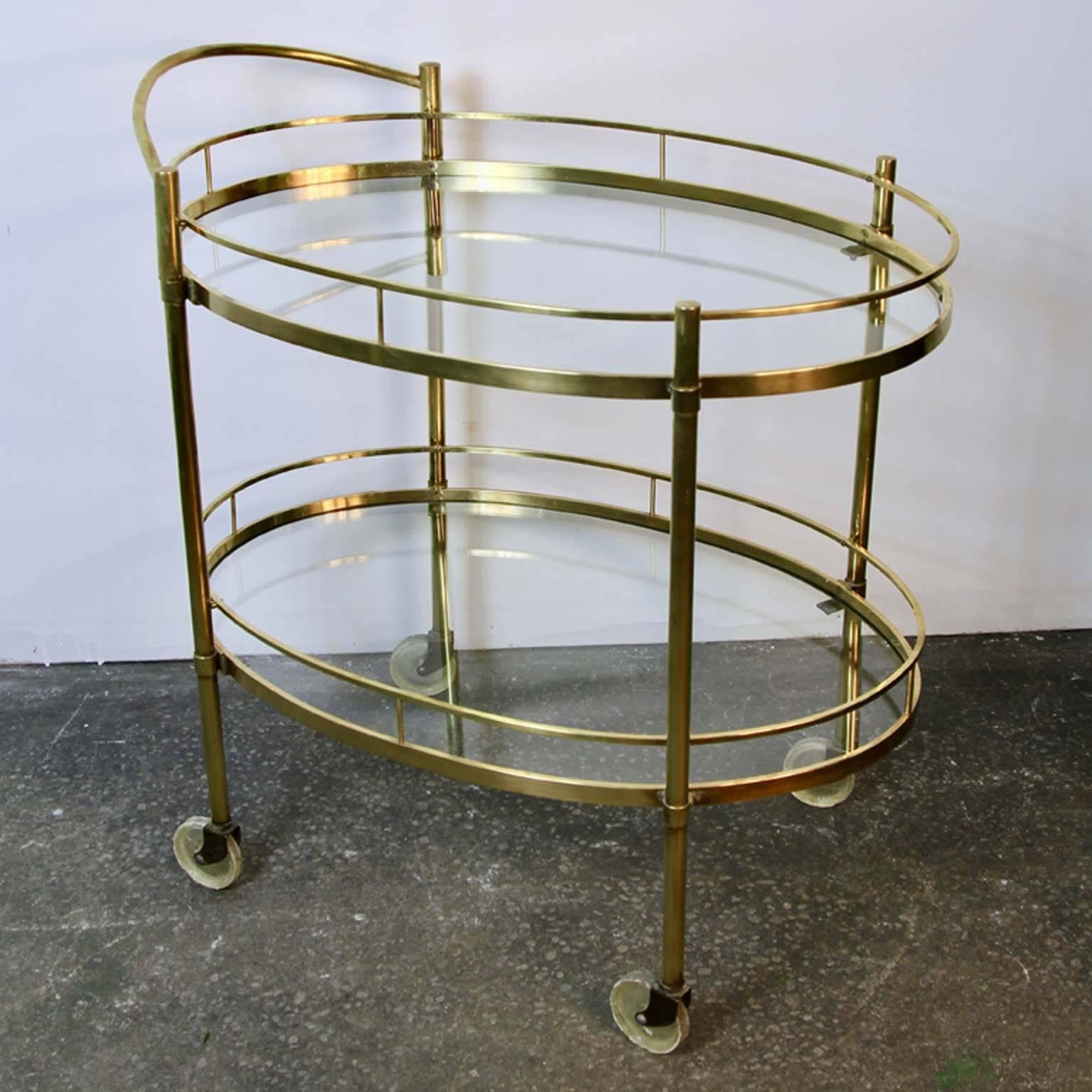 Beautiful brass bar cart with oval glass shelves. Brass in excellent condition, a few chips to the perimeter of the glass, can we replaced, or swapped with mirrored shelves. A nice blend of Mid-Century and Hollywood Regency style. Perfect accent
