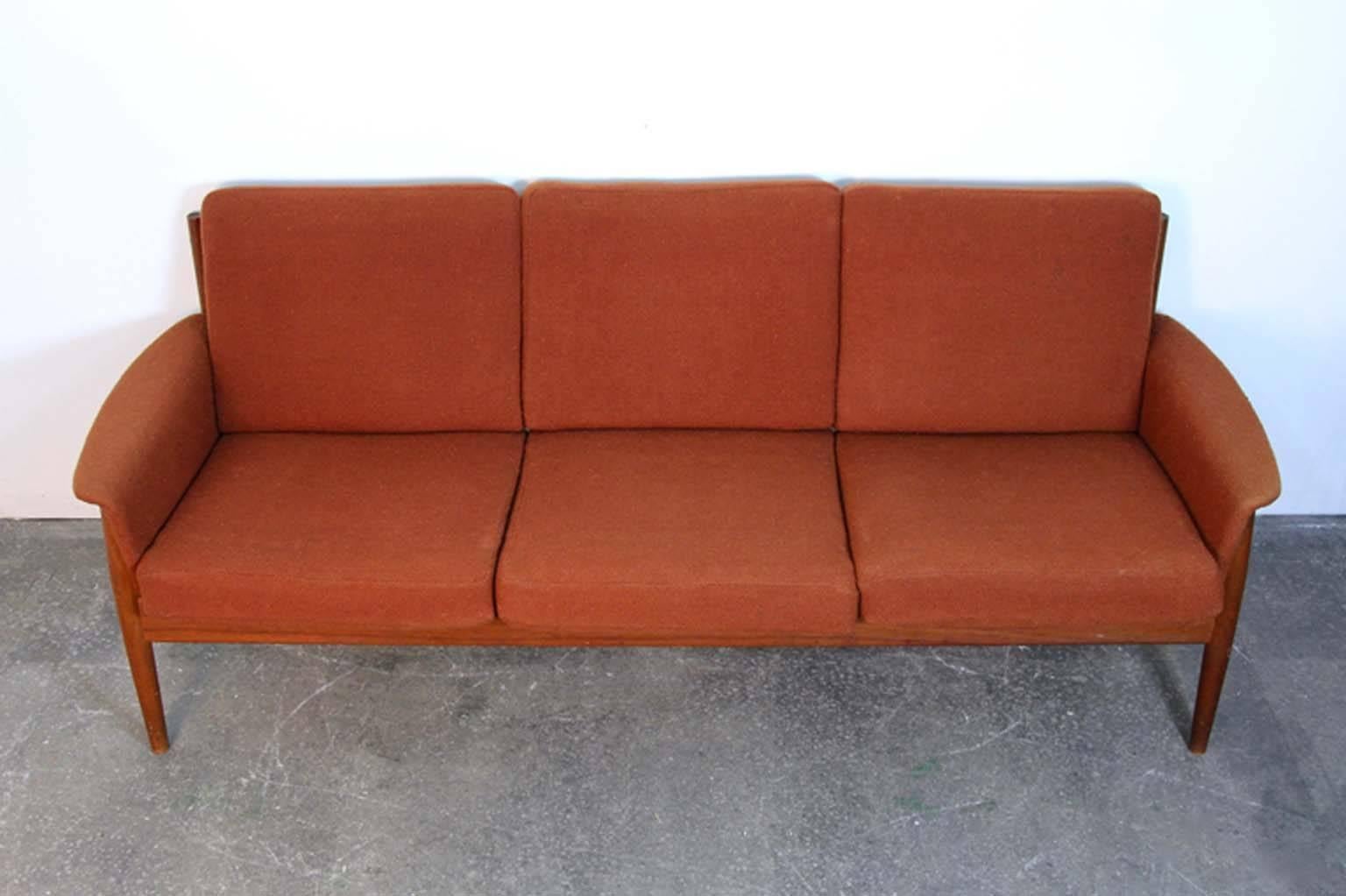 Grete Jalk teak sofa. Imported by John Stuart, labelled, three-seat sofa in original fabric. Has upholstered arms and cushions.