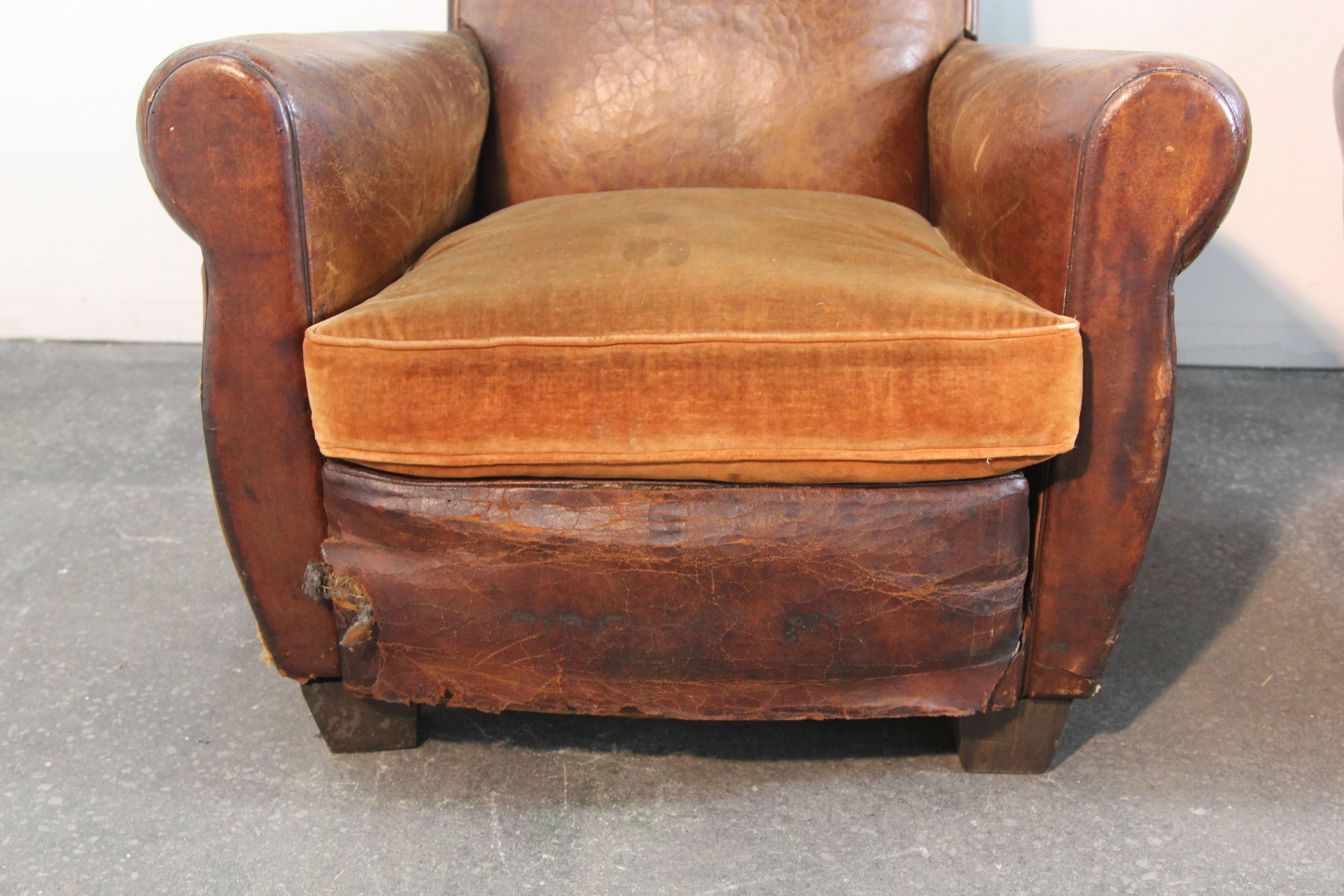 Incredible pair of original Art Deco style club chairs. In original distressed leather and velvet cushion. This is an assembled pair or chairs, as they do not match exactly, but they are very close and work well together. Distressed leather