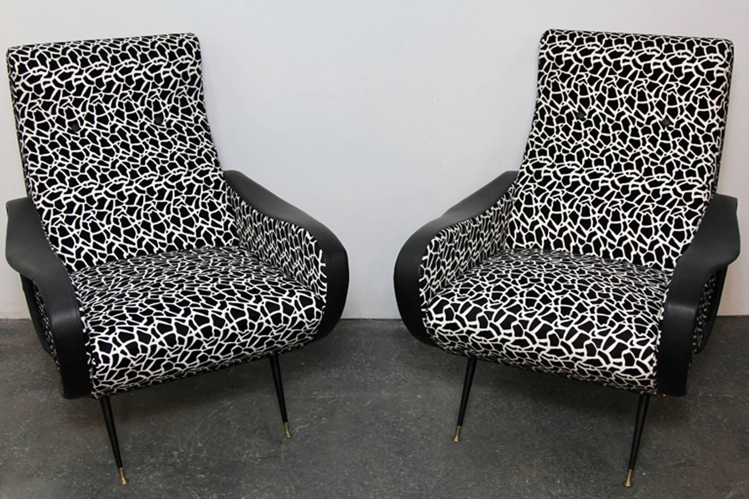 Contemporary exampled of Italian style Mid-Century Modern club chairs. Black and white funky fabric with leather arm details. Some scrapes and tears to leather on arms. Enameled steel legs with brass detail.
