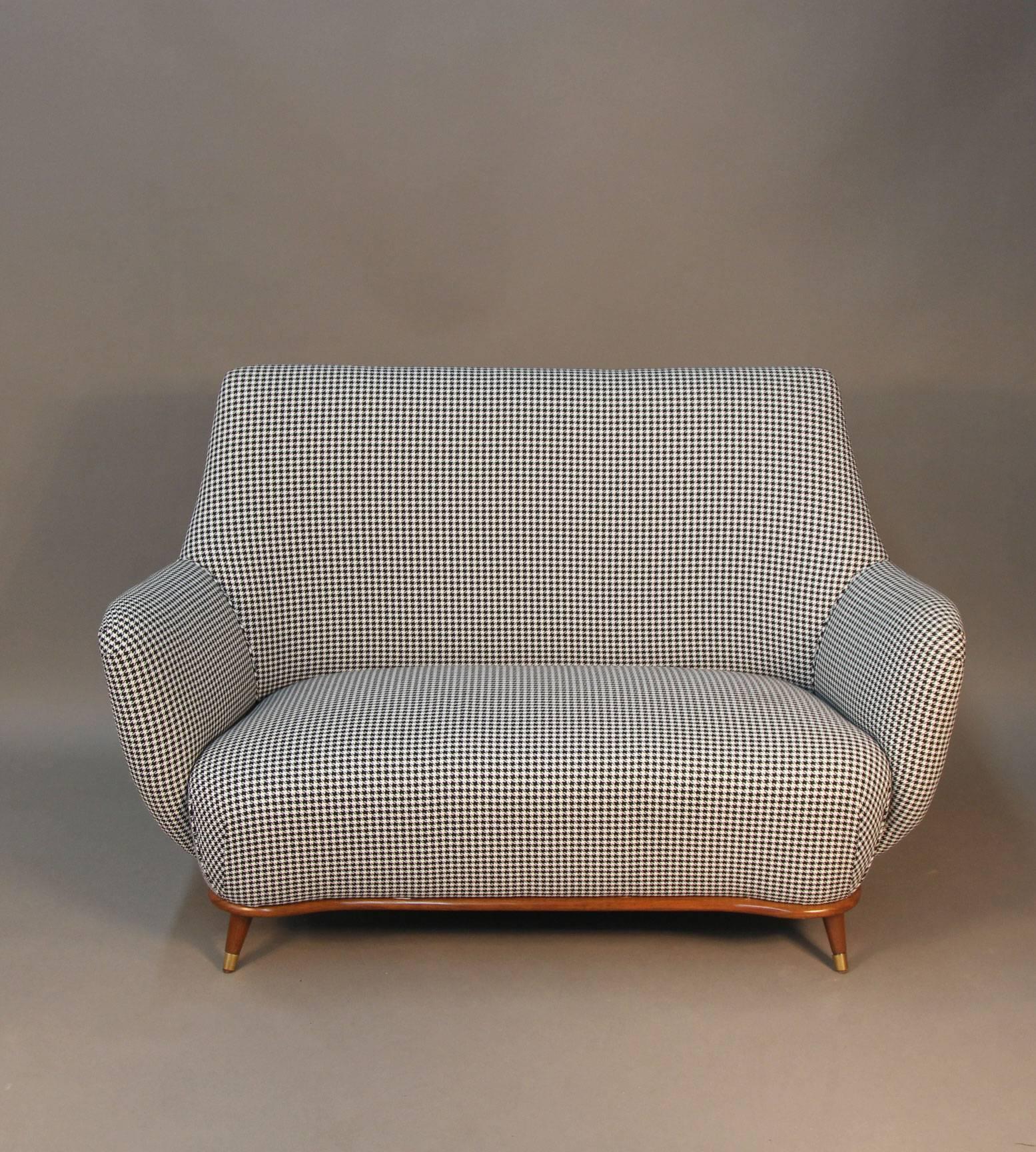 Mid-Century settee in the manner of Gio Ponti. Newly upholstered with houndstooth fabric in front, and black velvet pleated fabric in the back. Wood frame with new brass sabots.

Also available, matching armchairs.