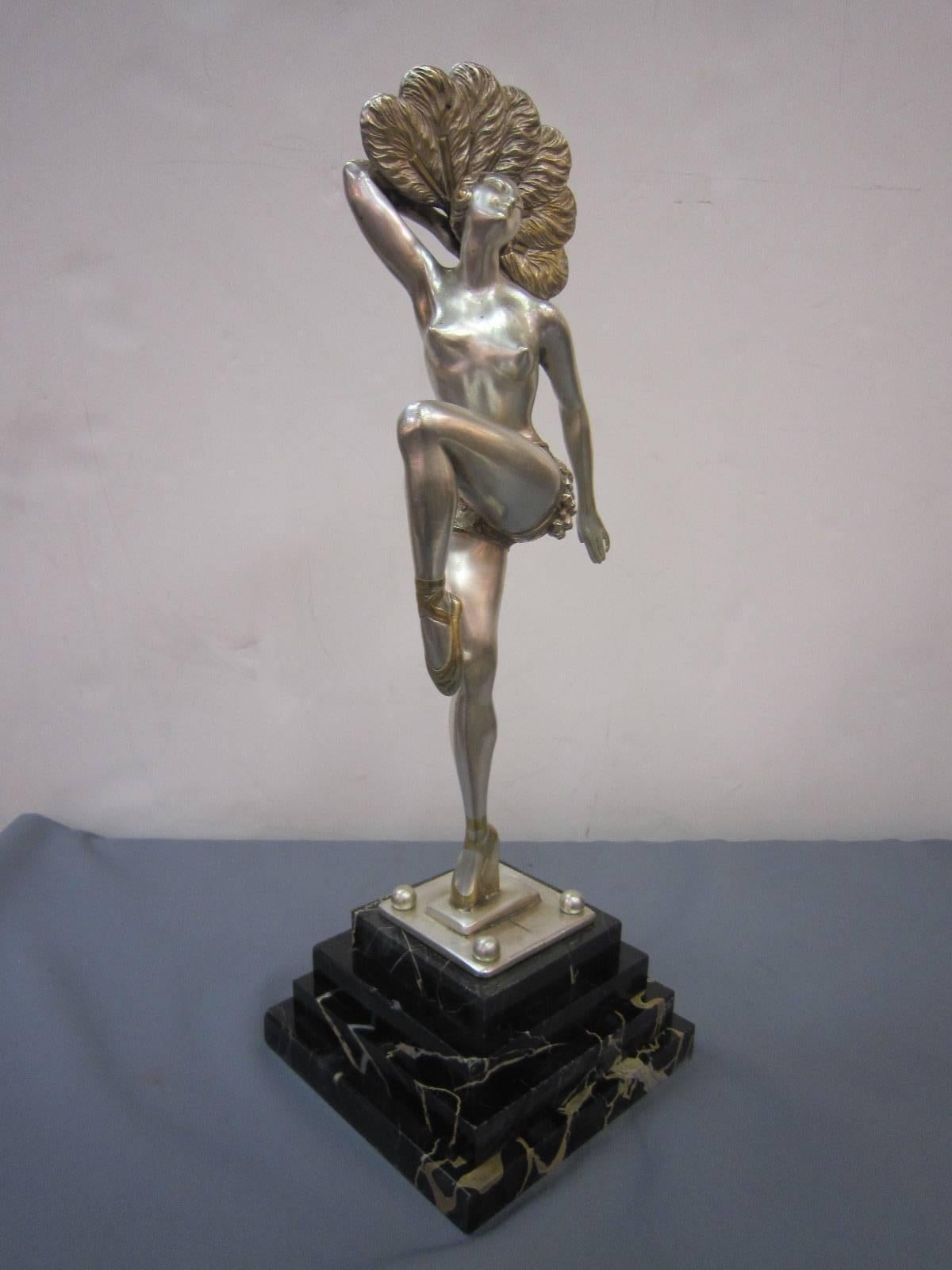 Original and graceful French Modernist statue of a female dancer with one foot up wearing ballet slippers and fashionable roaring 1920s garb. The figurine is finished in a silvered bronze with parcel-gilt accents and mounted on a stepped black and