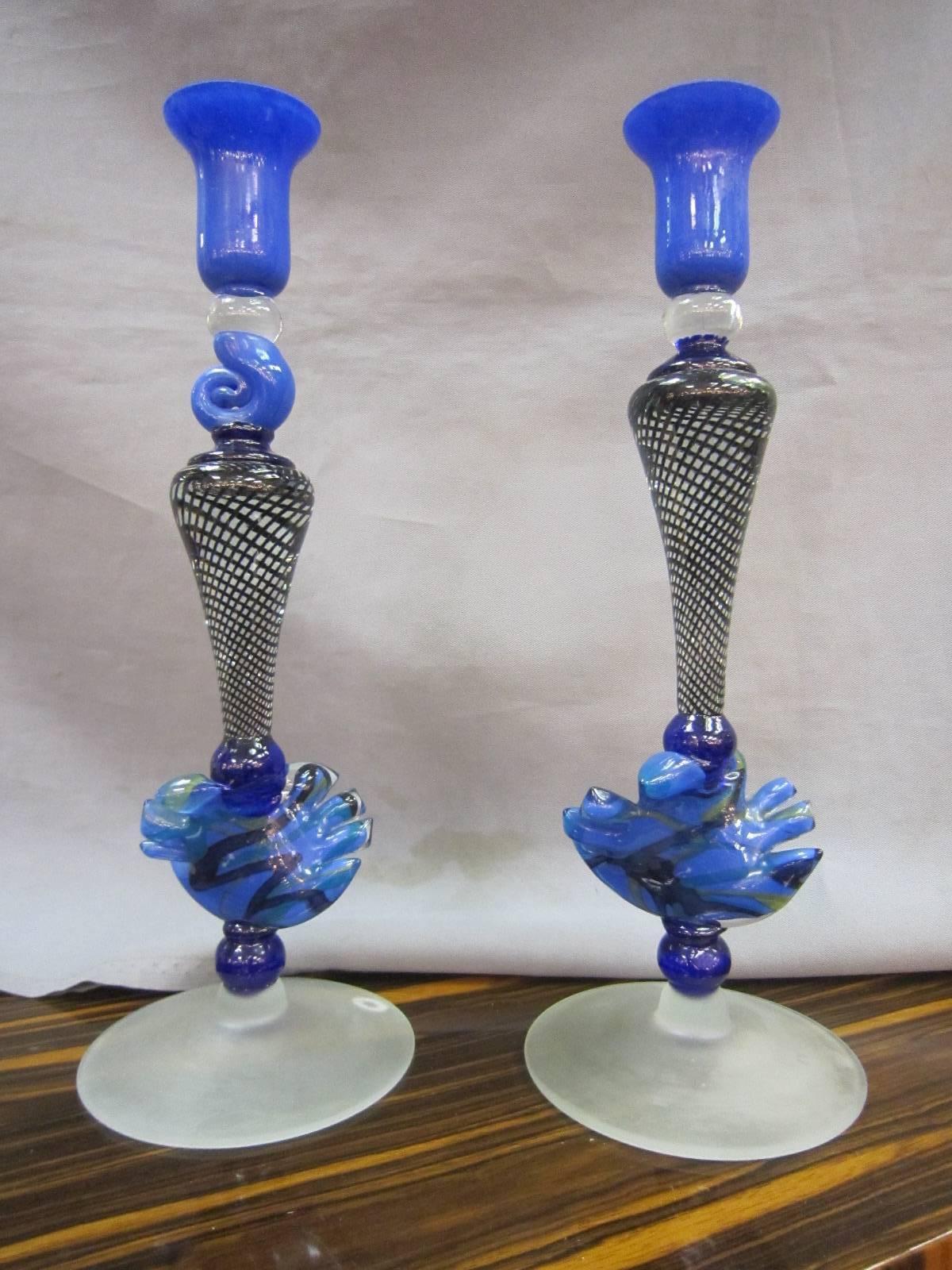 A similar pair of exceptional handblown cobalt, and clear candlesticks in various shades of blue with black lattice swirl ending in frosted feet. One candleholder has a blown snail form under the bobeche while the other has a taller flute, making