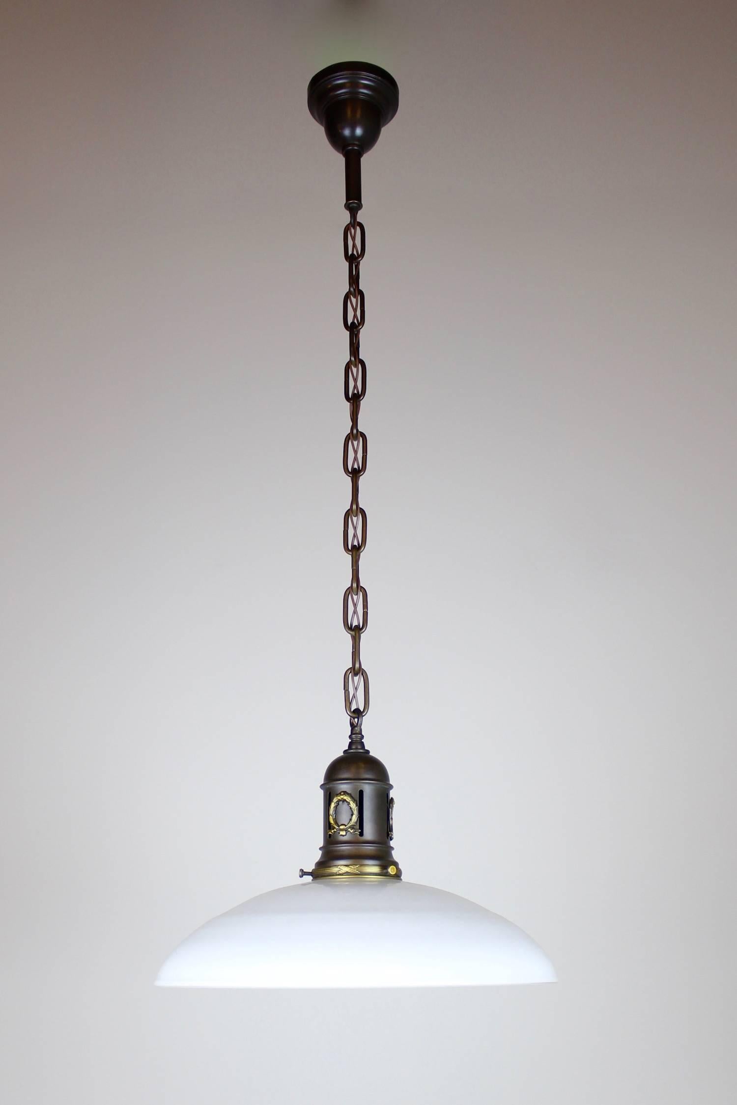These lovely antique pendant lights were sourced from a train station. Ideal for a kitchen island, and can be adjusted to spec, circa. 1915 Finished in a rich antique brown, featuring a small decorative wreath is satin gold cast brass. Lovely white