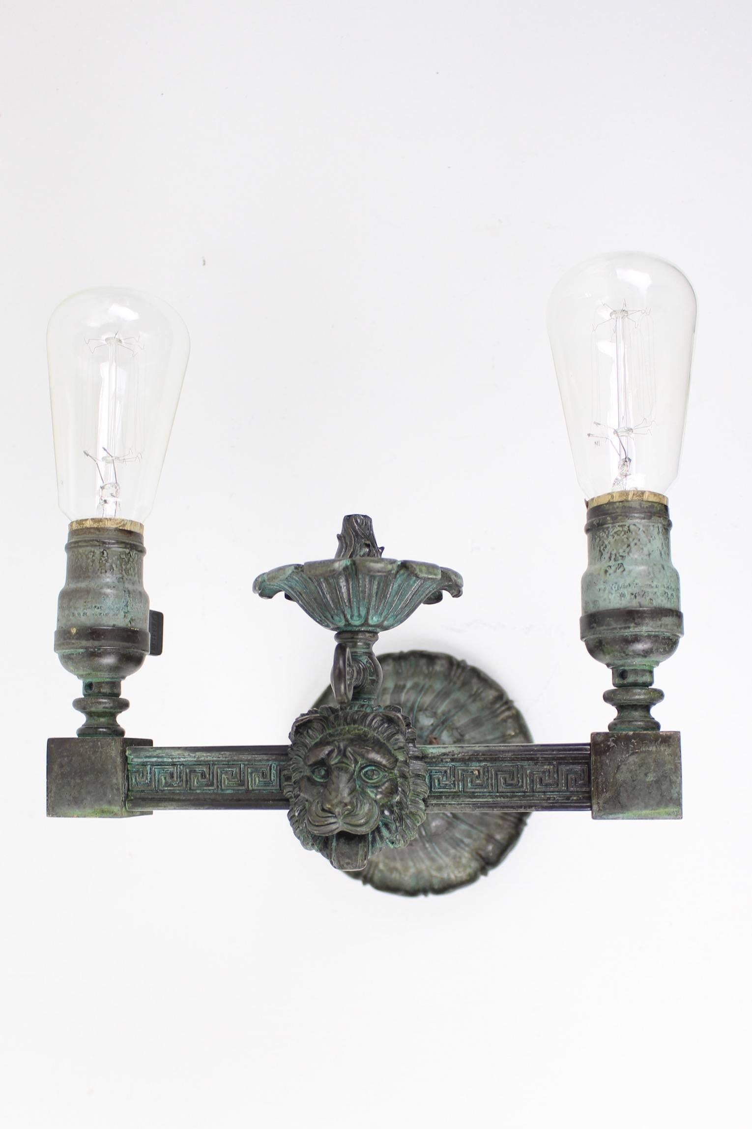 This pair of lion double-arm sconces feature a happy open-mouthed lion - tongue and all! Styled in Greek Revival with a 'Greek key' motif, circa 1910. Made out of cast and milled brass - heavy like bronze. Converted from gas to electric. These were