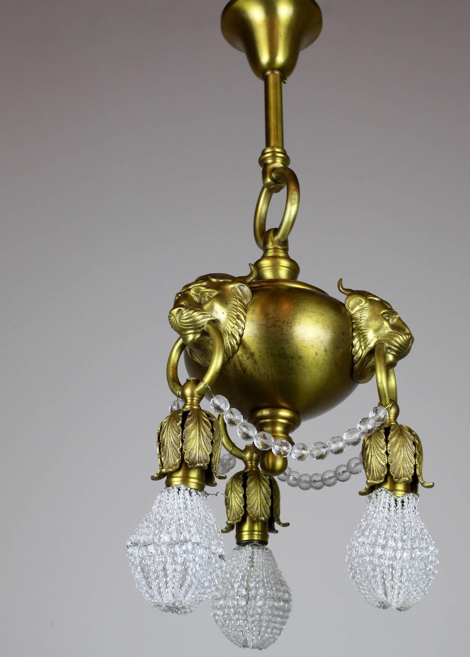 This is an absolutely charming - however petite fixture, circa 1910. Uncommon in size and superior in quality. This three-light chandelier is done in a neoclassical style using a 'lion mask' motif. 

Attributed to the 'Toledo Chandelier Company',