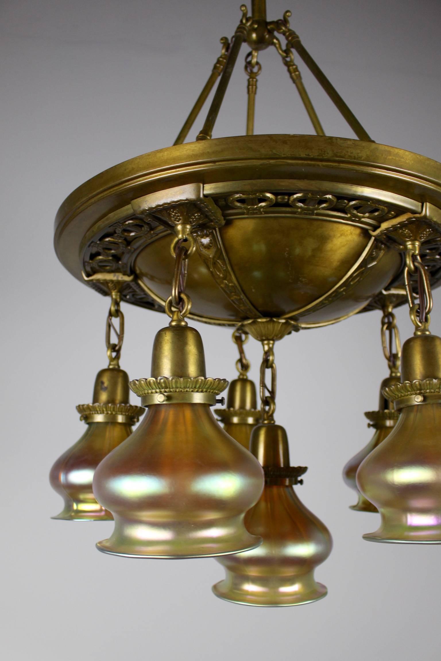An elegant pan fixture of a generous size, circa 1915. Beautiful brass castings decorate the body of this light fixture. Six lights in total - five hanging at the same level, with the central light staggered lower for depth. Art glass shades are in