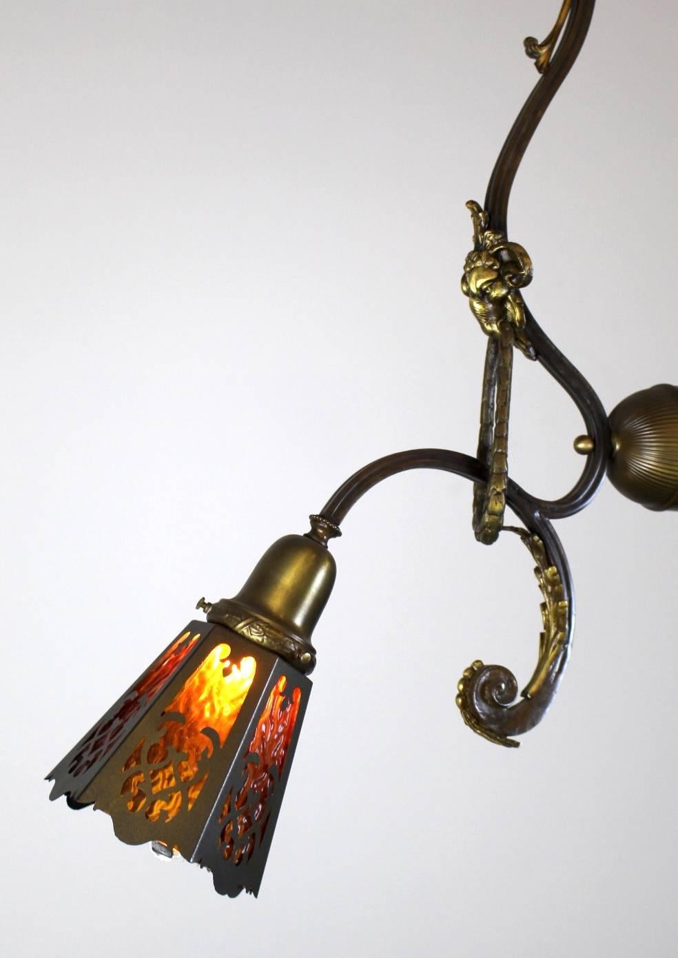 Unusual French Beaux-Arts style Fixture.

Two lights, fitted with cut-out shades with amber glass.

Great styling; includes ram's head details on each arm, holding suspended wreaths in their mouths.

Dainty leaves add shape to the expressively