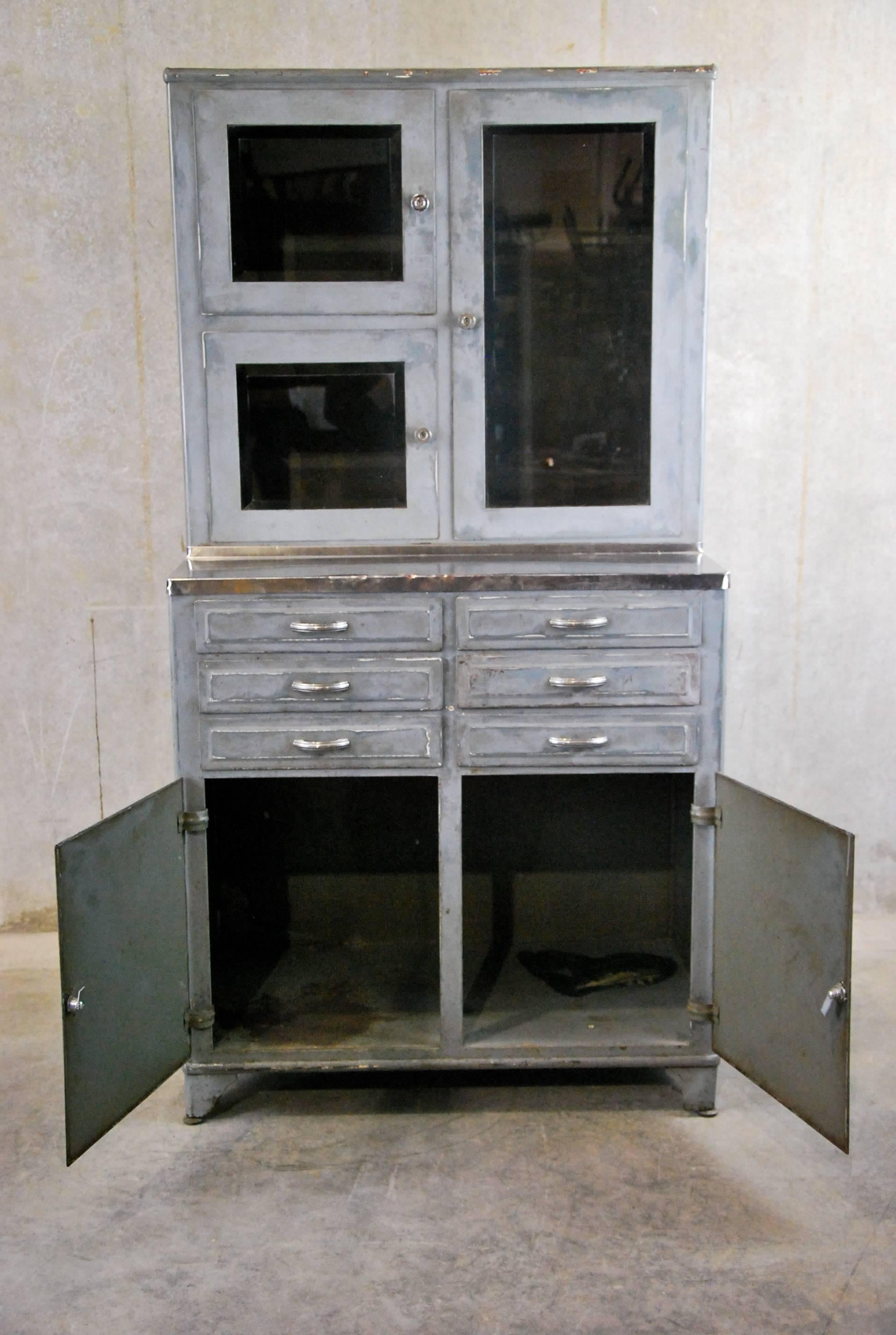 This well made piece retains an old painted surface over brushed metal with embossed drawers and doors. Feet are adjustable. Made in USA.
Complete with beveled glass doors and adjustable shelves, and stainless top.
Solid, clean and great simple