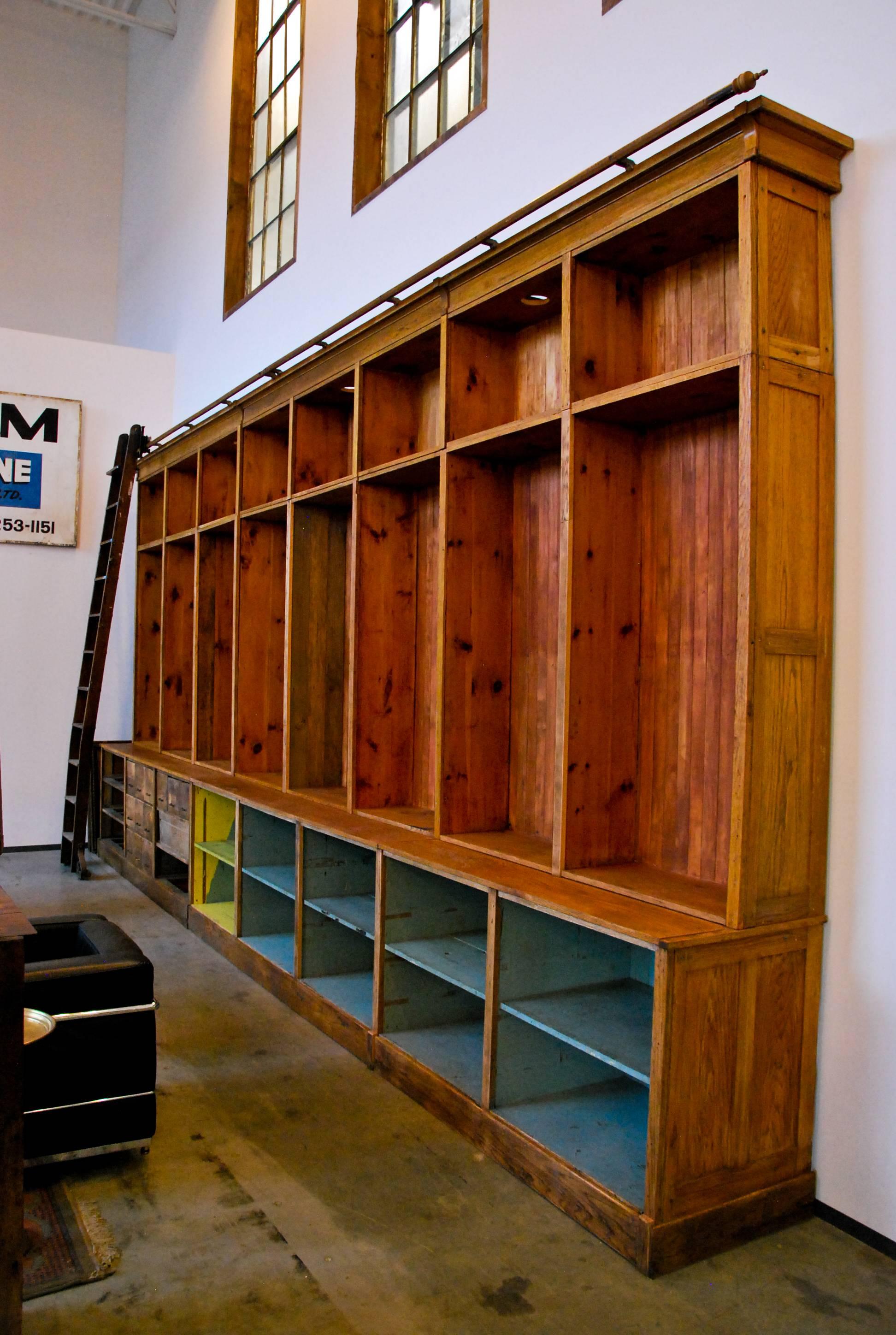 A fantastic 20-foot wide store cabinet with oak front, multiple compartments, and original rolling ladder and hardware. This unique piece was salvaged from a 1920 hardware store in Canada. The cabinet breaks down into sections for easier set-up and