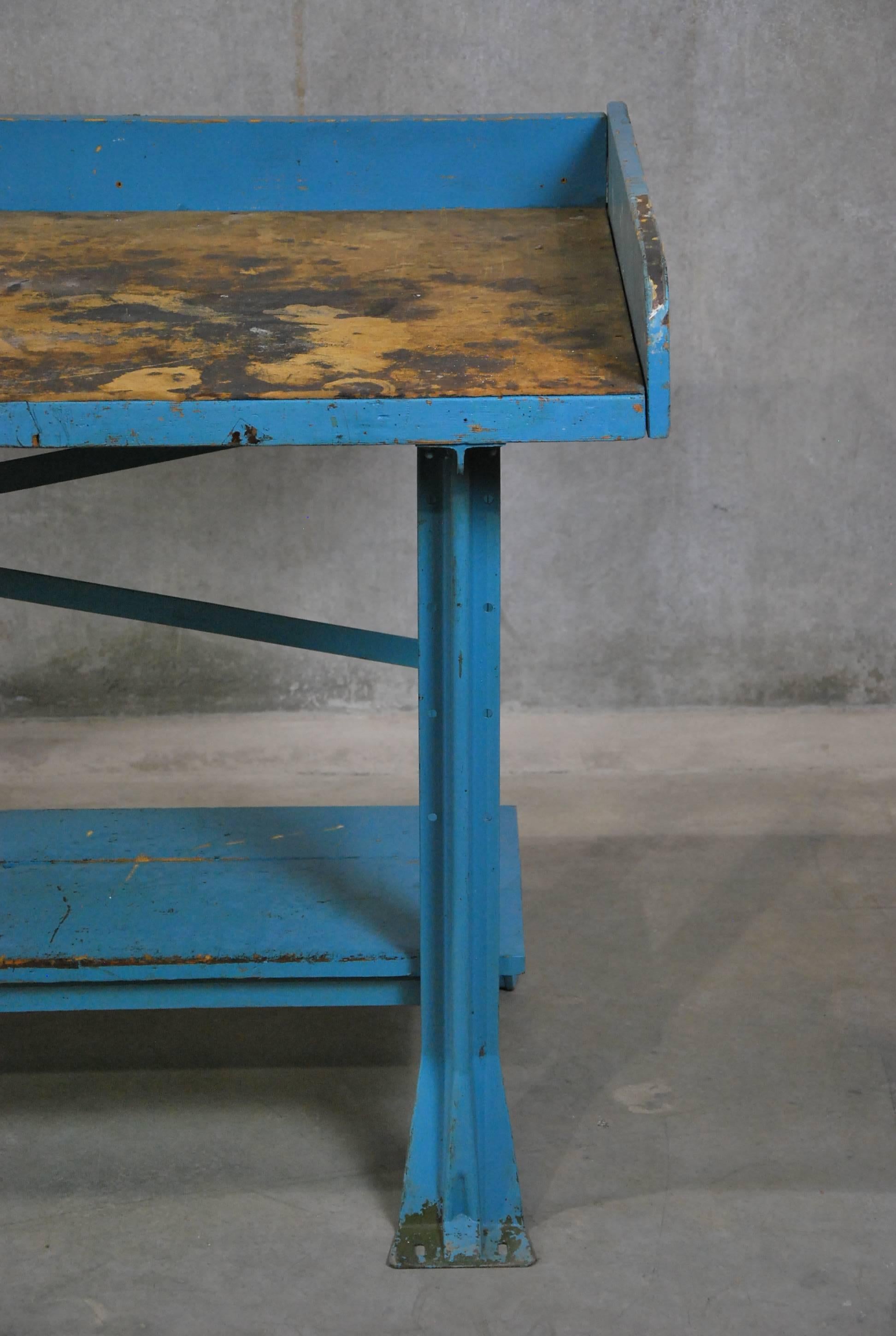 Industrial work table in old worn blue paint with removable top skirt. This piece has a wooden shelf, wooden top planks covered with particle board.
Found in a Chicago factory.