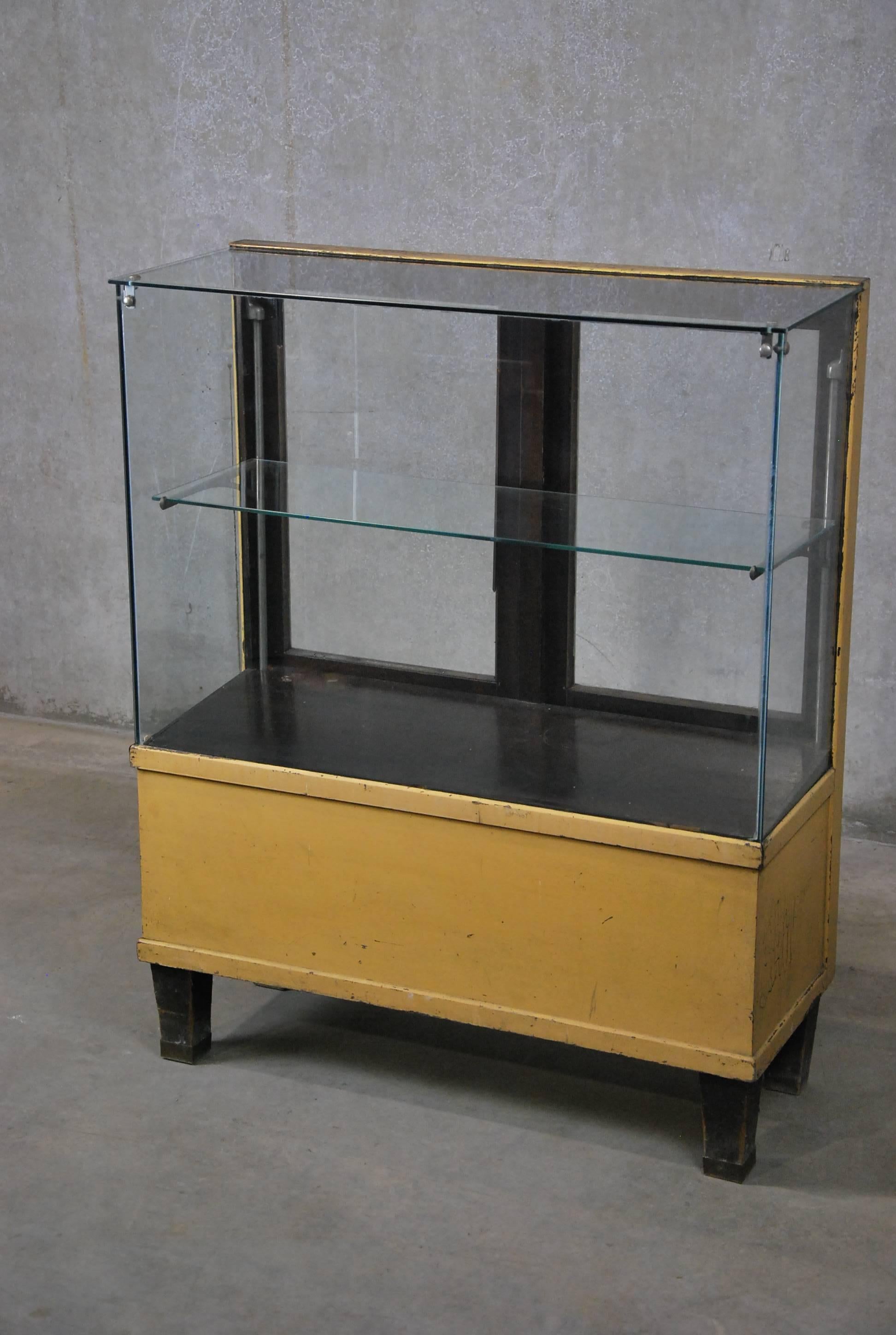 Small antique glass-and-oak display cabinet found in the American Midwest. Oak has overpainted, age-cracked polychrome surface paint. Features an adjustable glass shelf, plus a small storage shelf accessed from the back panel. Brass feet pads.
