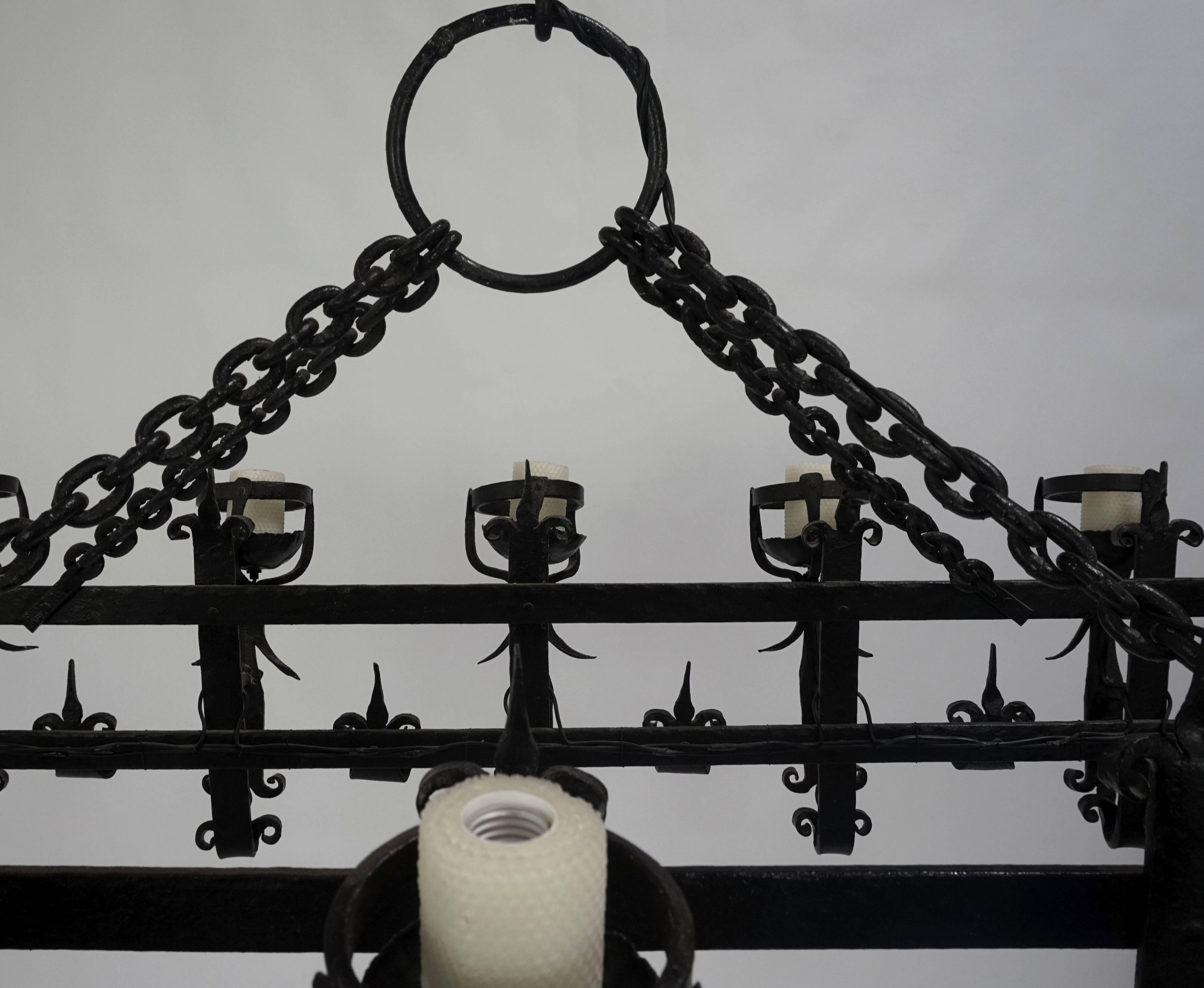 A heavy, iron chandelier in medieval revival and Henry III styles; hand wrought decoration, with honeycomb wax candle sleeves and heavy chain, 14 light. American, Beverly Hills, ca. 1915. Chandelier weighs 160lbs.