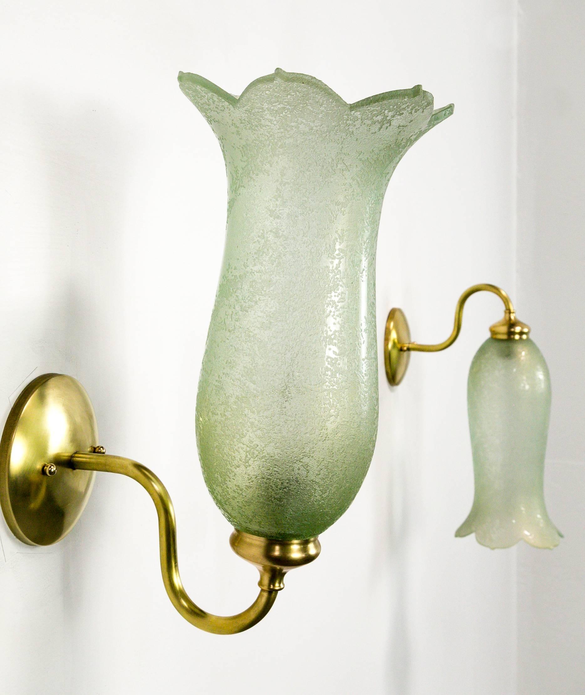 A pair of impeccably crafted, Art Nouveau bellflower shaped, textured, pale green glass shades made in the turn of the 20th century. They are mounted in clean and elegant, extended scroll arm brass. They have a timeless look that can fit a variety