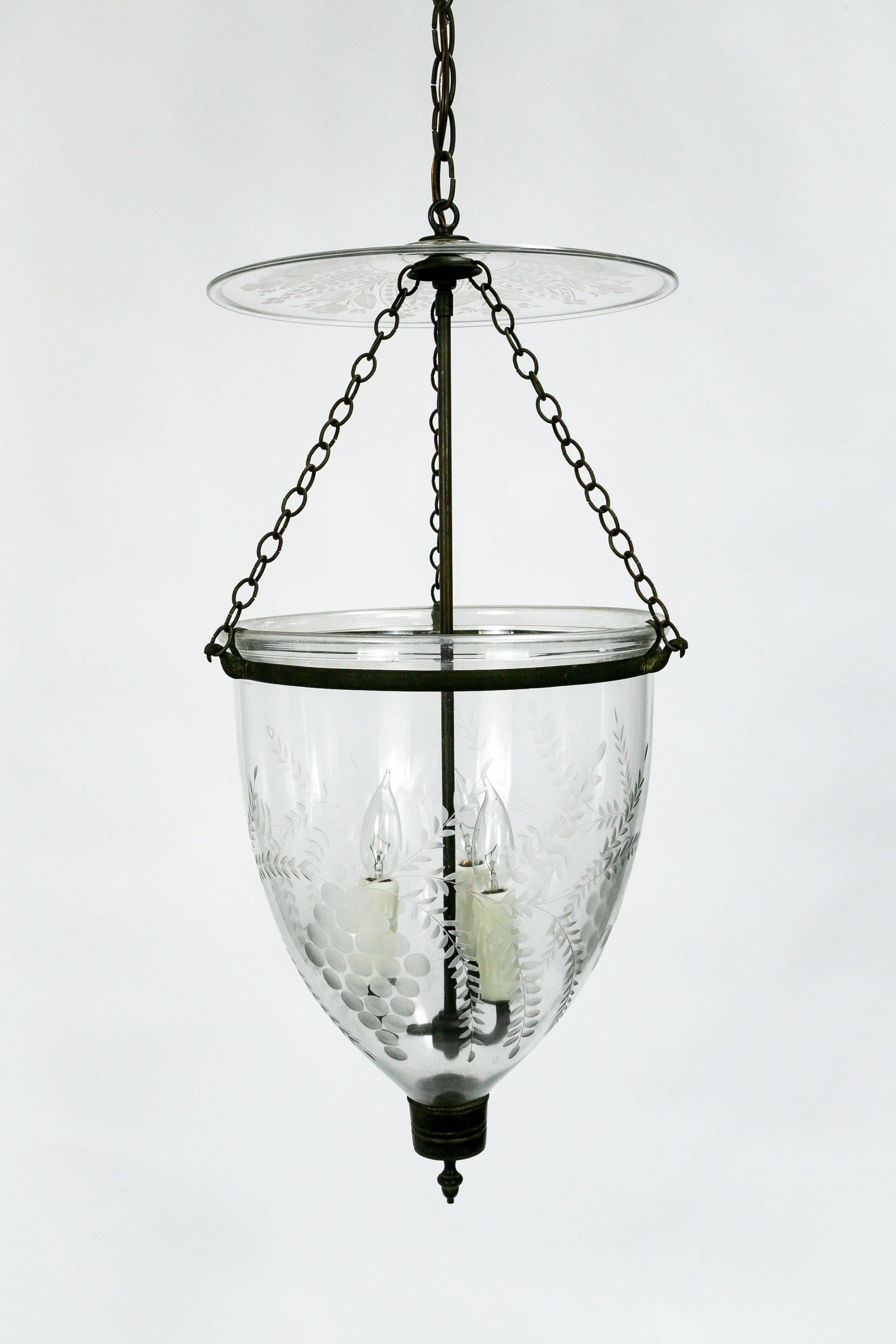 This Georgian style, bell jar pendant lantern is handblown and etched with a lovely, grape and leaf pattern. The etched smoke bell is particularly notable, with an intricate, flower design. The brass glass holder features bird chain hooks. The