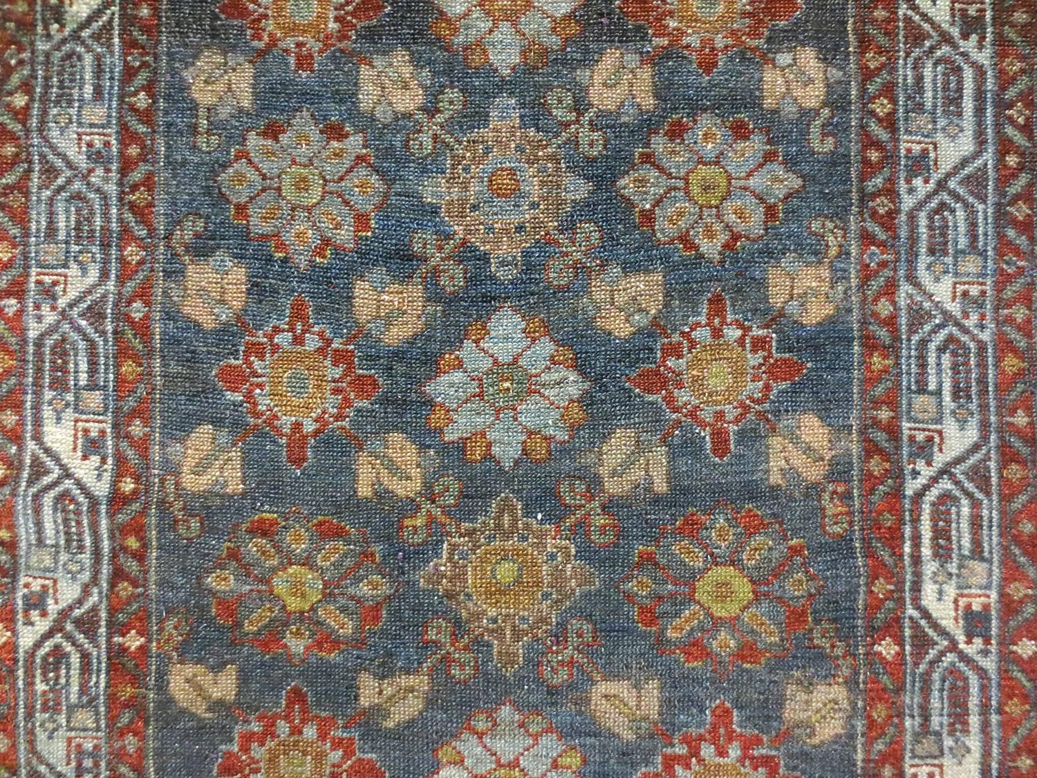 This is an antique Malayer, circa 1900s with a delightful viewing experience. This piece leads the eye down through a series of beautiful shapes and tones. It features a floral field on a cool blue background contrasting with warmer reds, yellows,