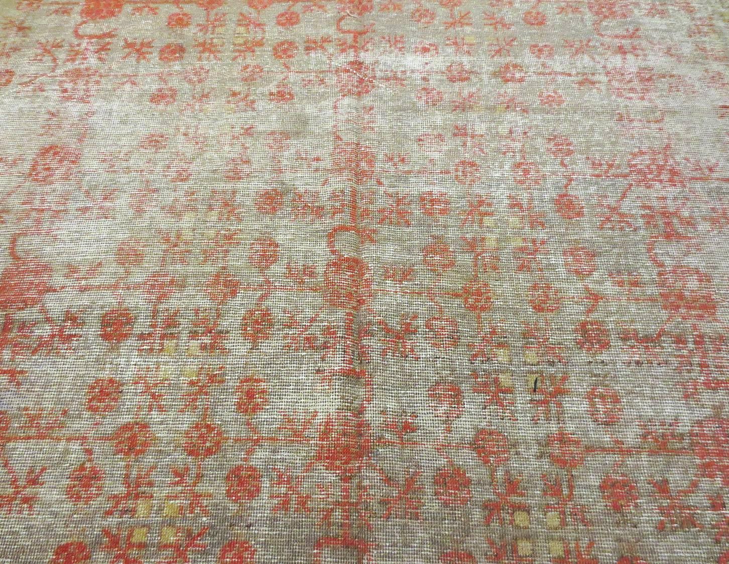 Dies ist ein antiker Khotan aus Ostturkestan, ca. 1880, der gleichmäßig abgenutzt ist. Der Teppich ist mit einem zarten roten Granatapfelmuster überzogen, das einen schönen Kontrast zu einem gedämpften, erdigen Hintergrund aus Gelb-, Elfenbein-,