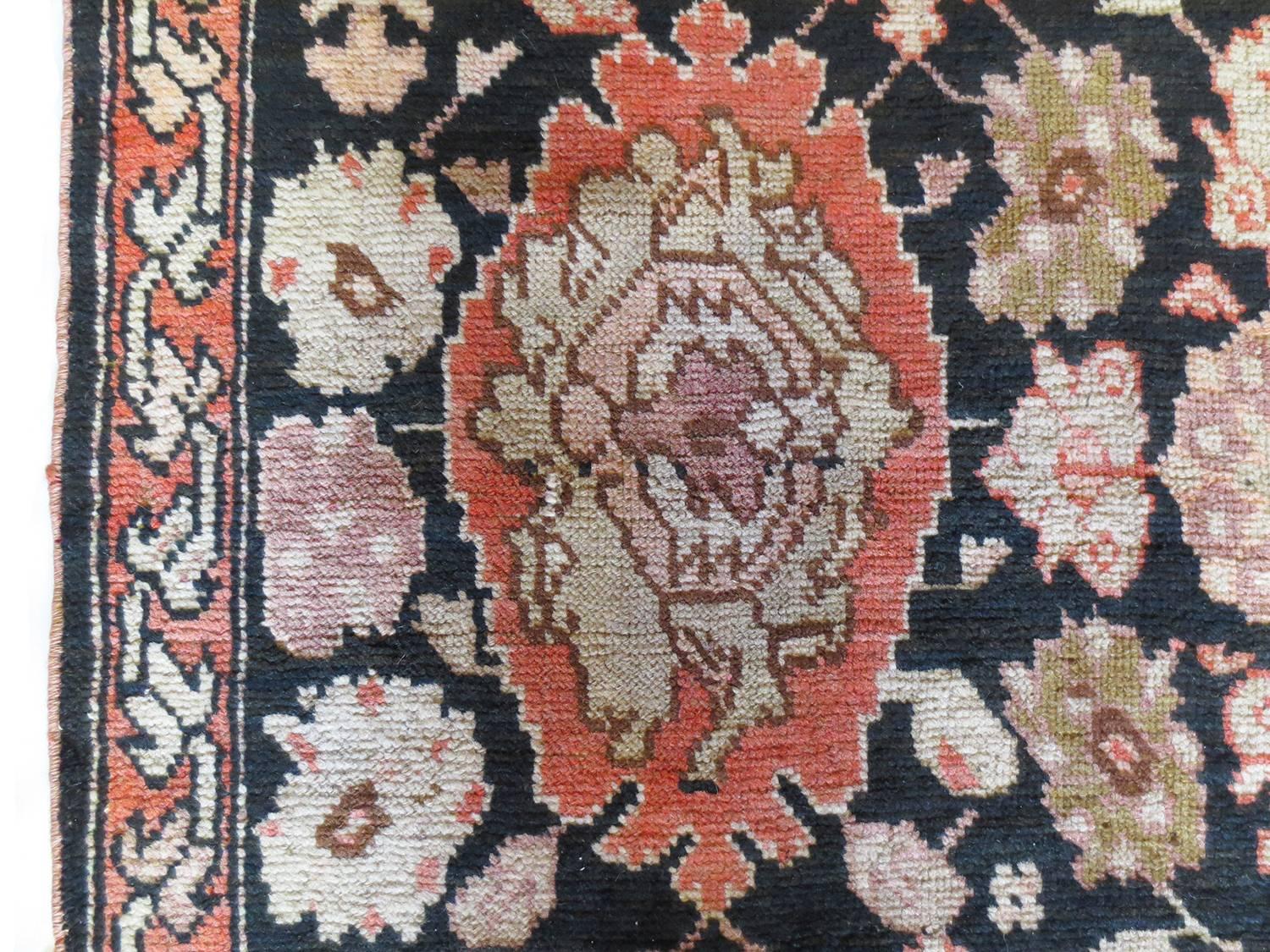 This is an antique Karabagh runner, circa 1880s. It features geometric motifs and rosettes filling the field on a black background with shades of salmon reds, ivory, pink, olive green. A thin border allows for the field to dominate and take canter