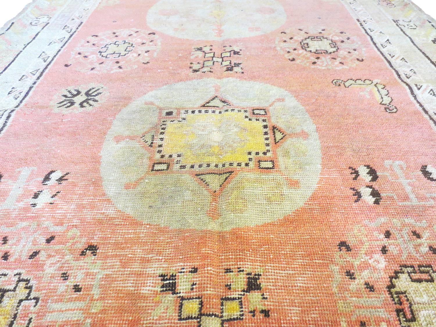 This is a lovely antique Khotan rug is from East Turkistan. Three stylized medallions is set against a soft coral field surrounded by a border of clouds. Depictions of pomegranate, along with butterflies, and other symbolic motifs also fills the
