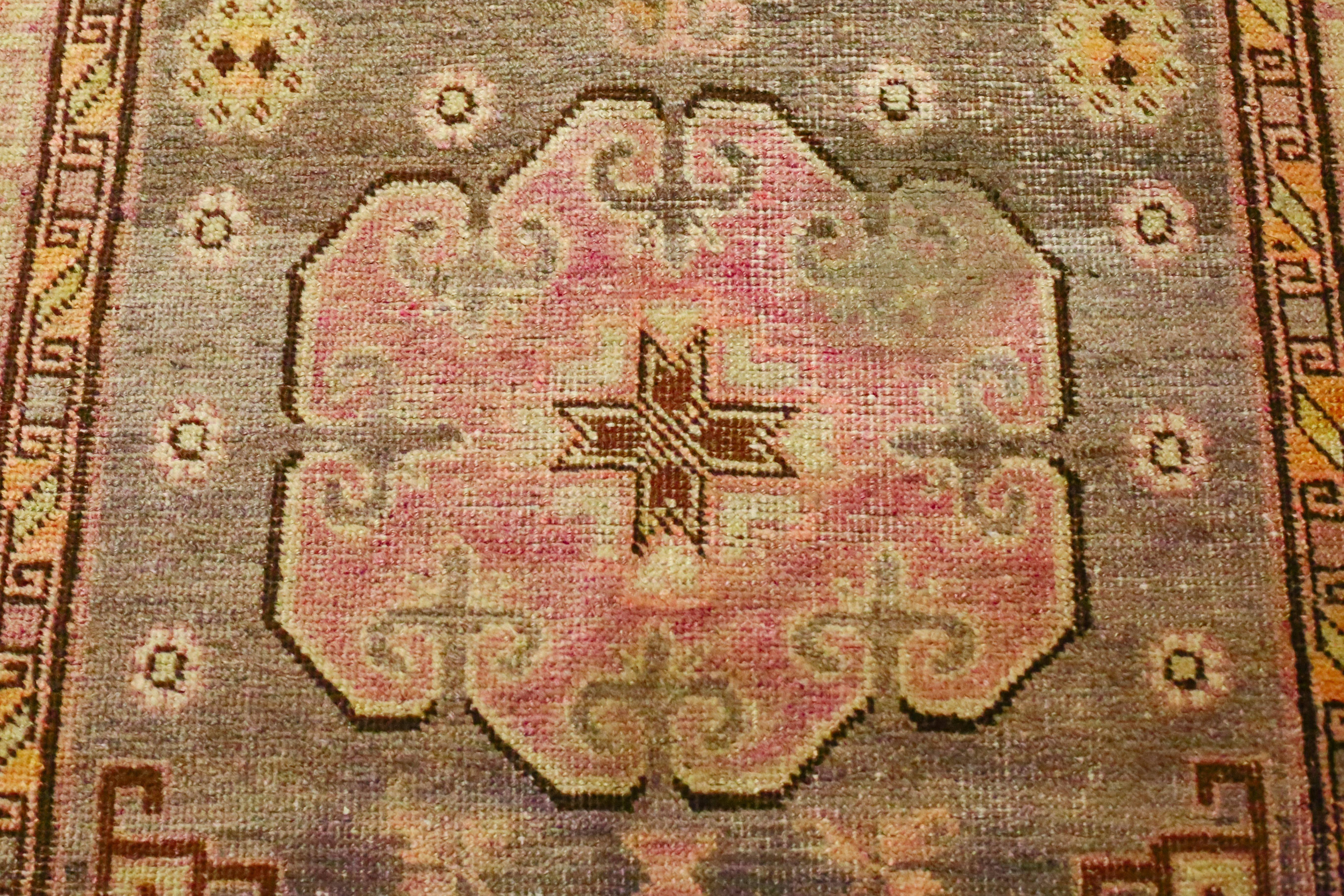 This is an antique Khotan rug from East Turkistan circa 1880s. Three cloud-like central medallions are set against a field of stylized floral forms. Multiple borders frames the field, each with different designs and symbols. Shades of pinks, olives,