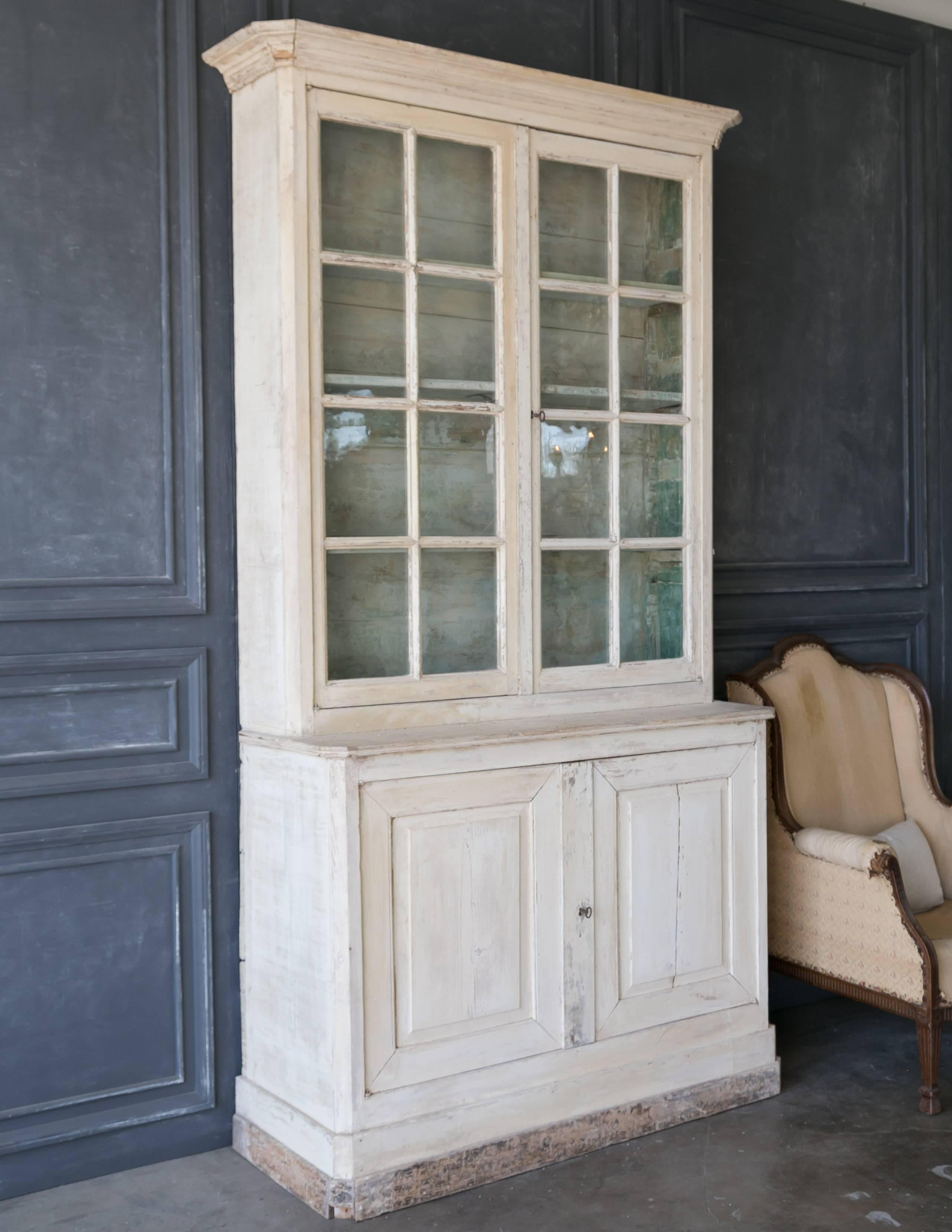 Dazzling antique French cabinet in pine with distressed ivory finish exterior and original aqua green interior. Three narrow shelves in the glass display part and one shelf behind the doors. This tall cabinet has a crown molding and functional keys