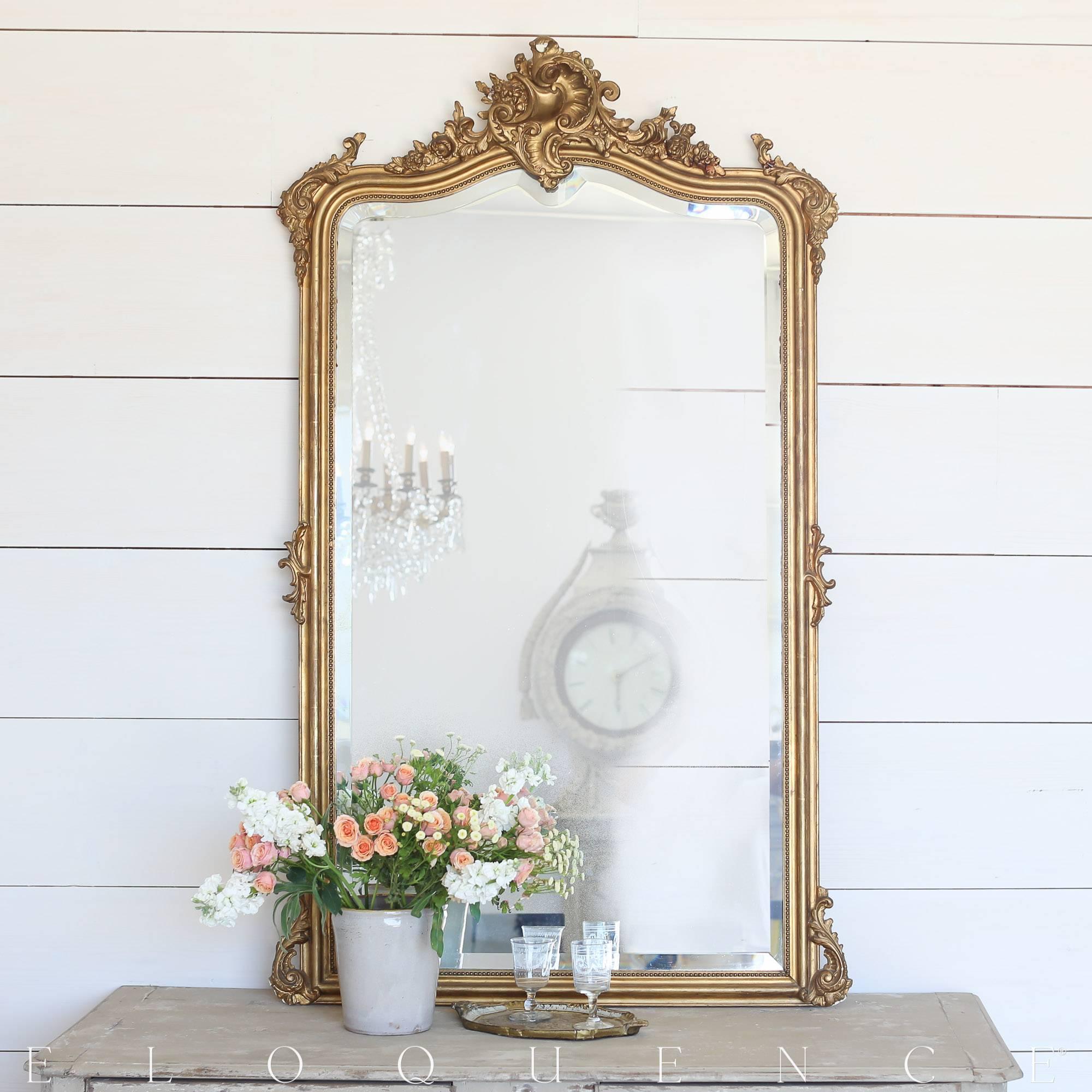 Stunning antique Louis Philippe floor mirror with ornate, floral carved crest, original beveled glass, and delicately roped border in a distressed gilt finish. Touches of umber reds whisper throughout the gilt and add old world charm to a bedroom,