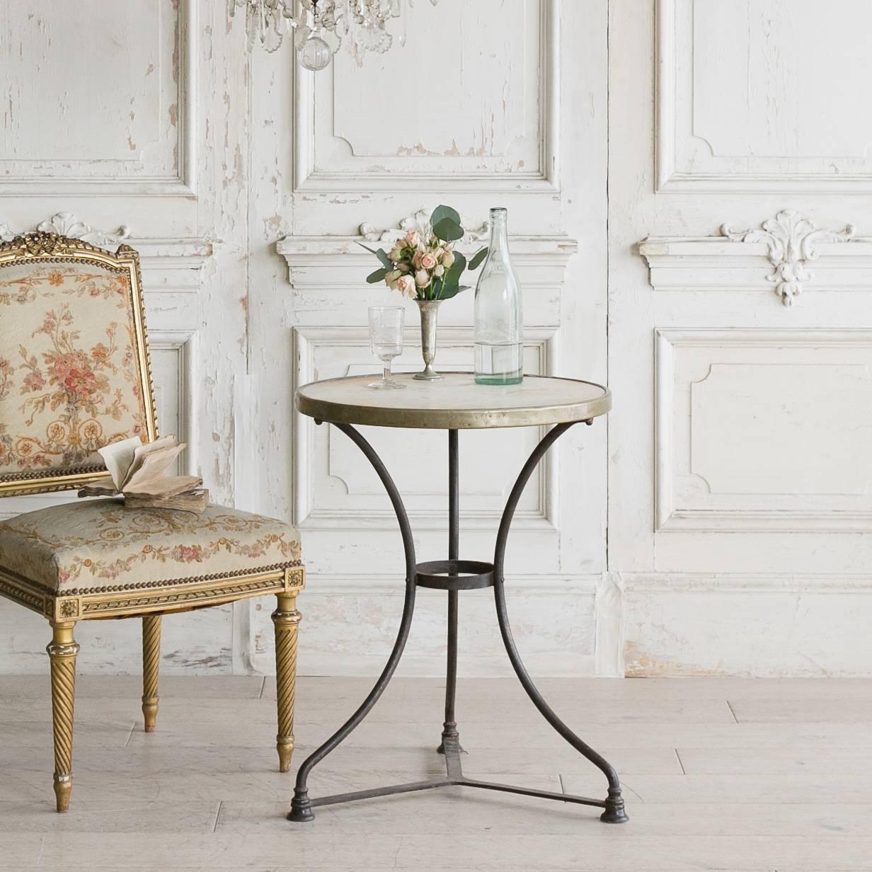 Antique Parisian cafe table with marble table top and iron base. Brass colored metal surrounds the marble and connects to the iron base. A simple tripod stretcher holds the legs together. This piece is perfect for a small balcony, as a riser for a