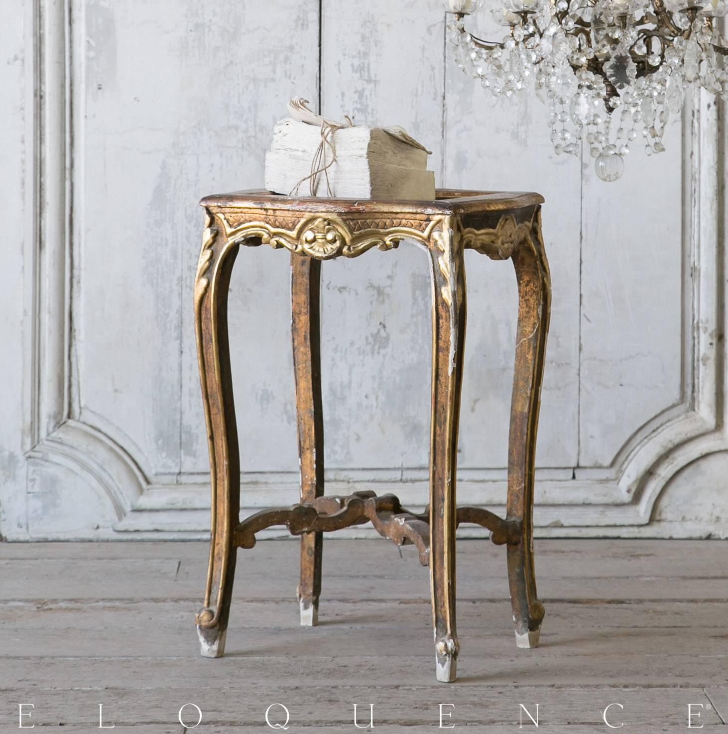 Single lovely Louis XV style vintage side table finished in a darkly patina, gilt and distressed to reveal the original brick red undercoat. Hand-carved fleur de lis and floral outlines add elegance and charm. This piece is topped with a perfectly