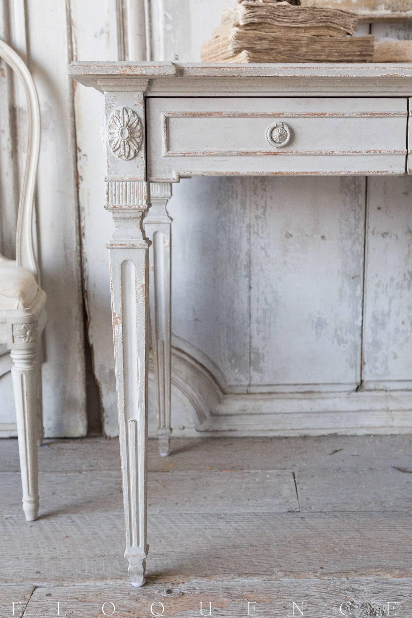 Eloquence® Herra writing desk in Gustavian grey finish. This piece shows off Classic lines adorned with delicate carvings, all finished a soft neutral tone that will compliment any living space. Lovingly worn at the edges and featuring two spacious