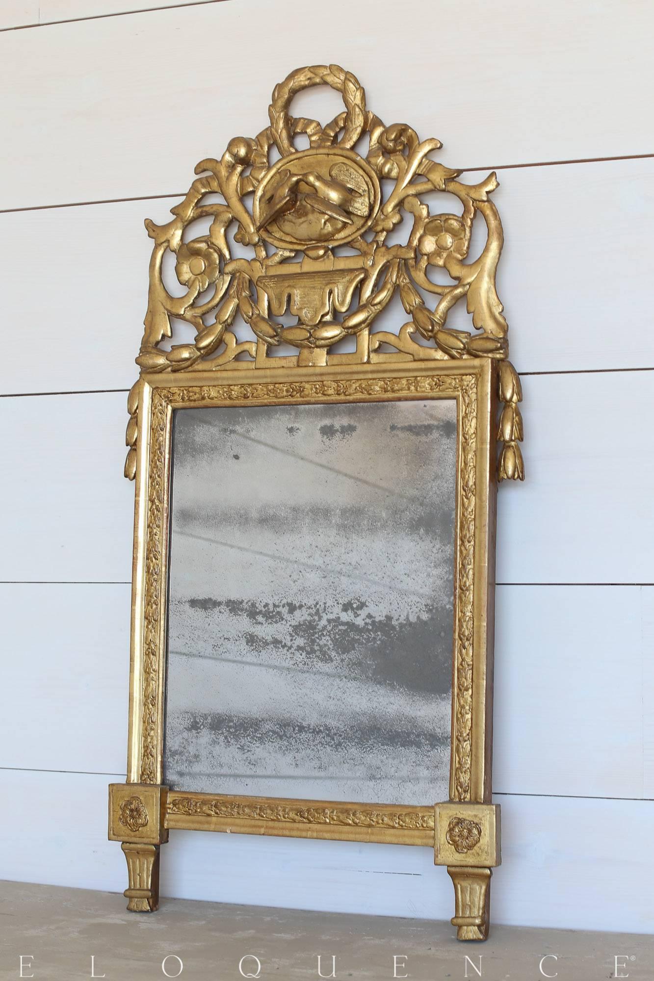 A petite wreath, sweet kissing birds and a floral motif decorate the crest of this antique mirror. The lightly distressed gilt finish and original mercury glass truly add to the aged elegance of this piece.