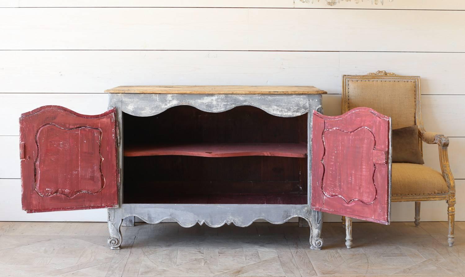 French antique sideboard in a gorgeous distressed gray with a natural wood top. Two carved cupboards open to a washed crimson interior with contrasting and functional lock and key closure. A single interior shelf offers storage perfect for a guest