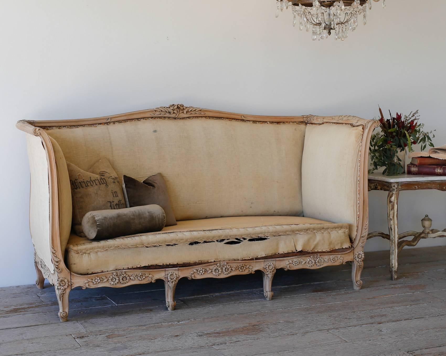 Incredible high-backed Louis XV daybed in a soft, bleached oak finish. Gorgeous floral details adorn each arm and crest while subtle curves of the frame add romance to this large-scale piece. The daybed has beens tripped back to its original muslin