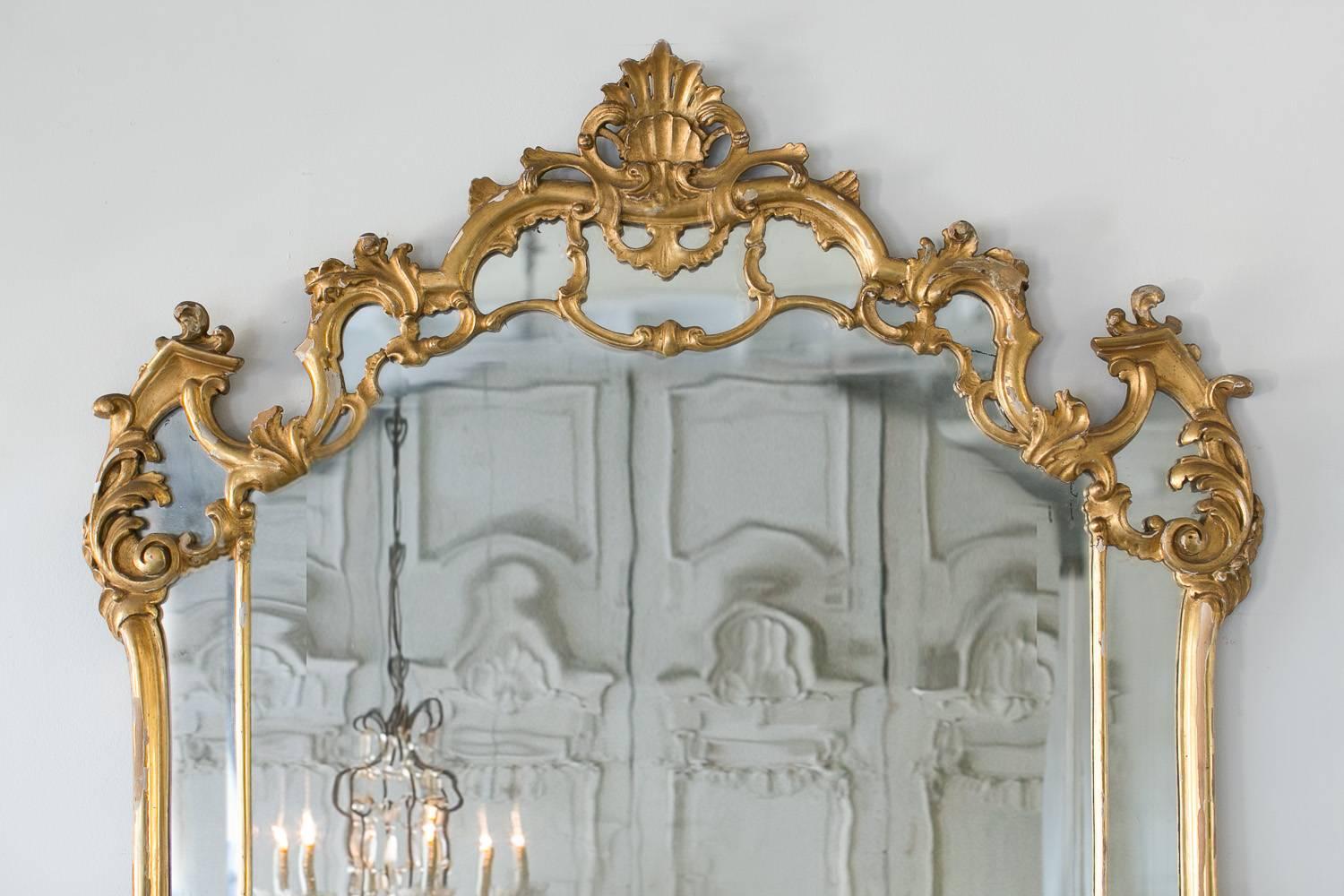 Regal antique mirror in muted gilt. Delicate carvings mimic the waves of the ocean leading to a shell motif at the height of the crest. The original glass comes with imperfection however the light scratches and distortion in parts add to the age of