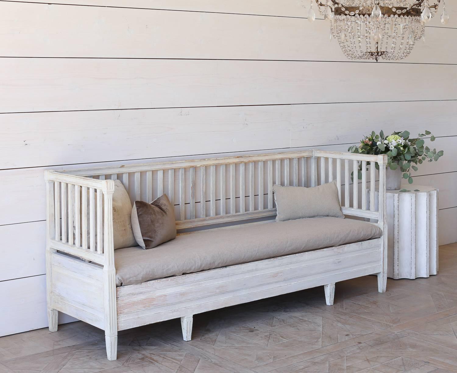 Charming antique Swedish day bed in white washed finish. Remove the mattress and raise the seat to find a small storage area. This classic country styled piece is sure to lend luxury to a sun room, porch, or entry way.
