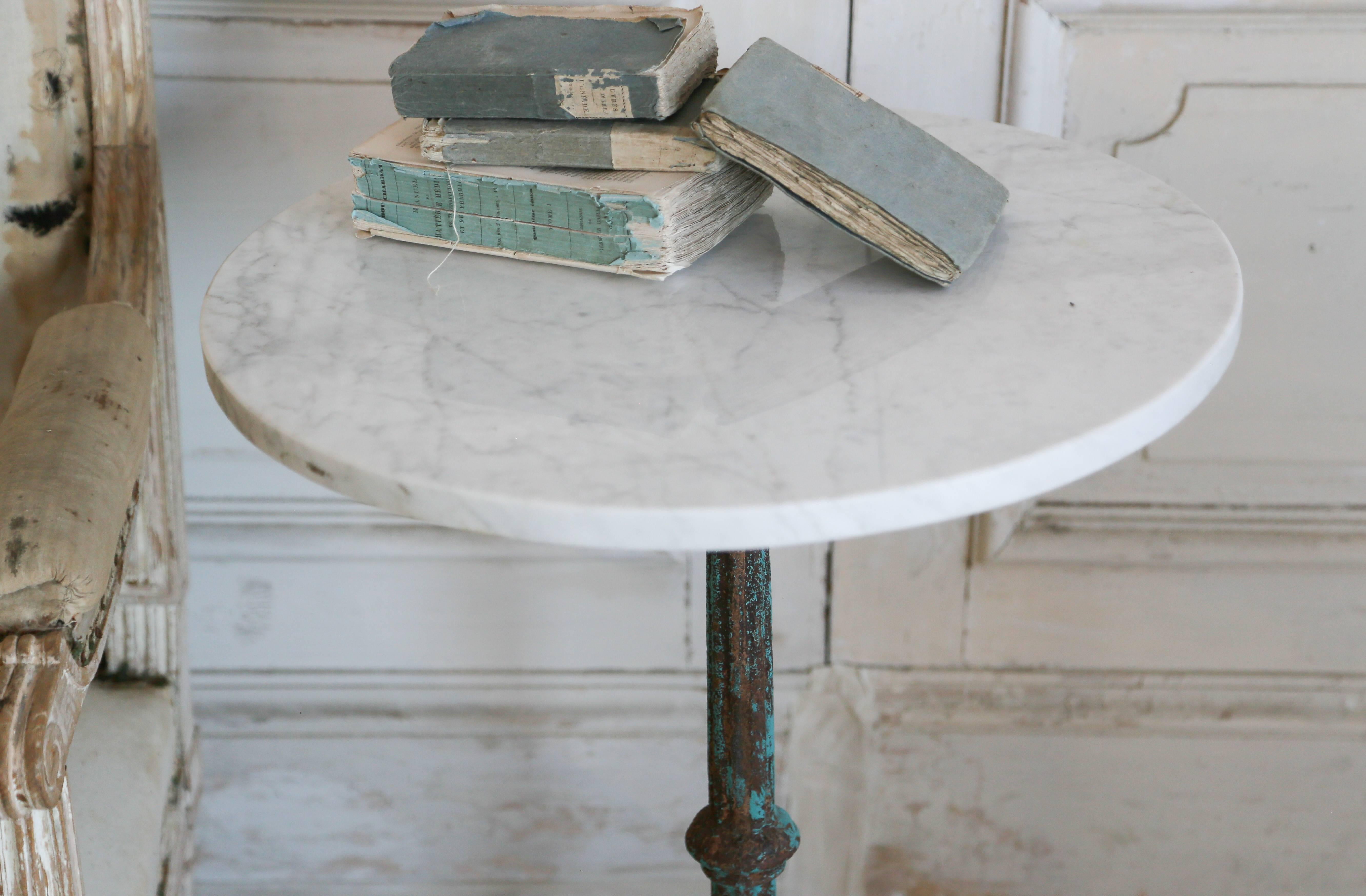Adorable pair of bistro tables in distressed, turquoise iron with light Carrara marble tops. The pedestal leg is balanced by a tripod base decorated with swirls and ocean motifs. The tables inspire intimate conversations over a cup of coffee or