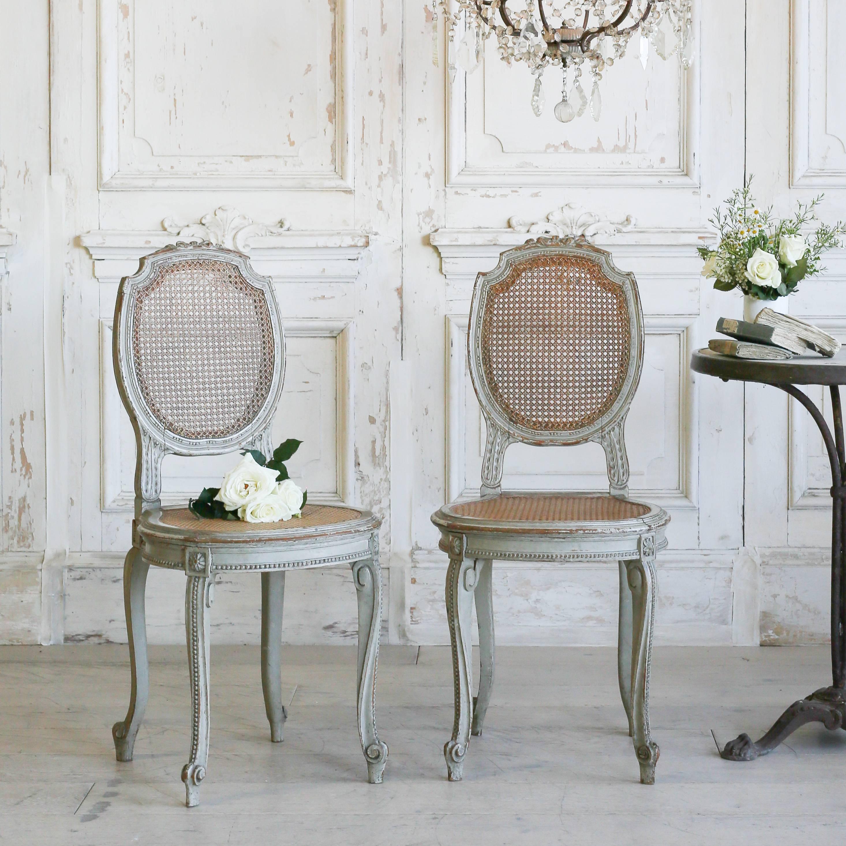 Gorgeous pair of antique side chairs with cane seat and back. These delicate chairs in distressed duck egg finish feature delicate carved beading down the legs, around the apron and surrounding the back rest frame. High, poised feet add to the